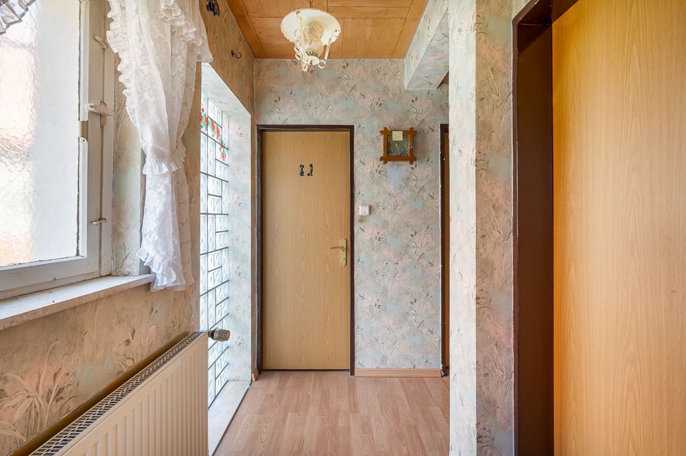 Heller Flur mit Holztüren, Blumendekor und Fenster mit weißen Gardinen.
