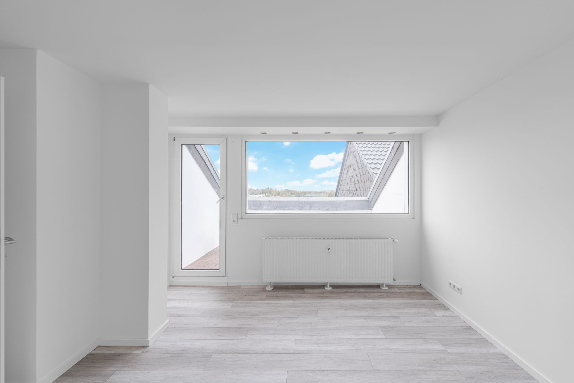 Heller, leerer Raum mit großem Fenster, Tür zum Balkon und weißem Heizkörper.