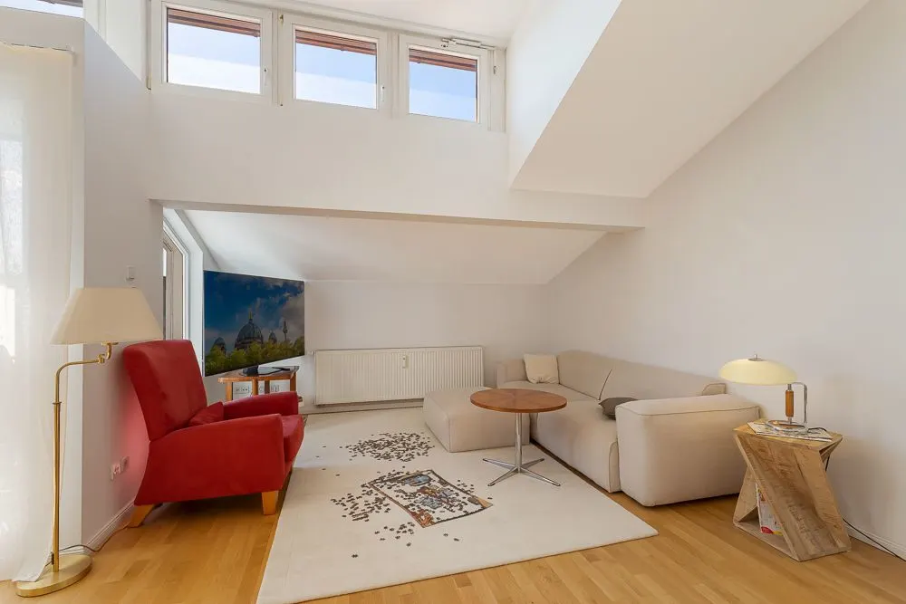 Helles Wohnzimmer mit rotem Sessel, beiger Eckcouch, Stehlampe und Couchtisch auf Teppich.