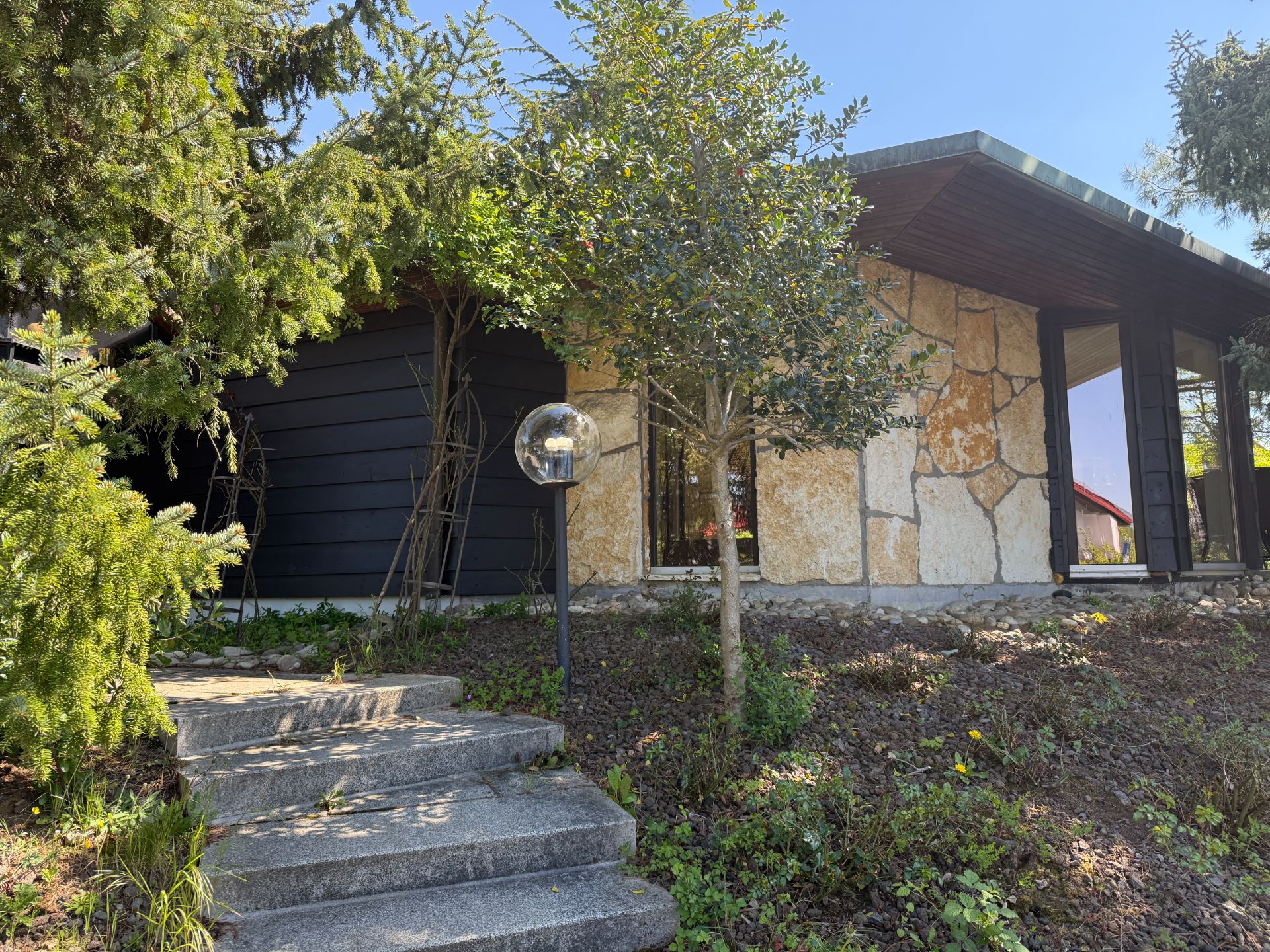 Außenansicht eines Hauses mit Natursteinfassade, Treppe, Bäumen und Garten.