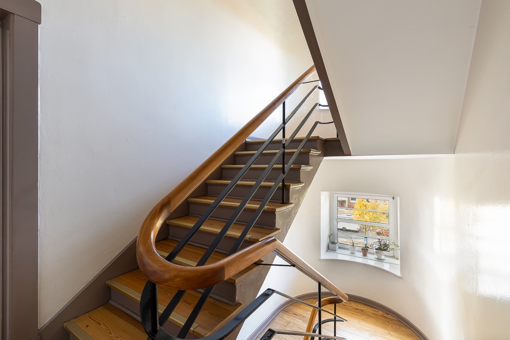 Treppe mit Holzhandlauf und Fenster mit Pflanzen, Blick nach draußen.
