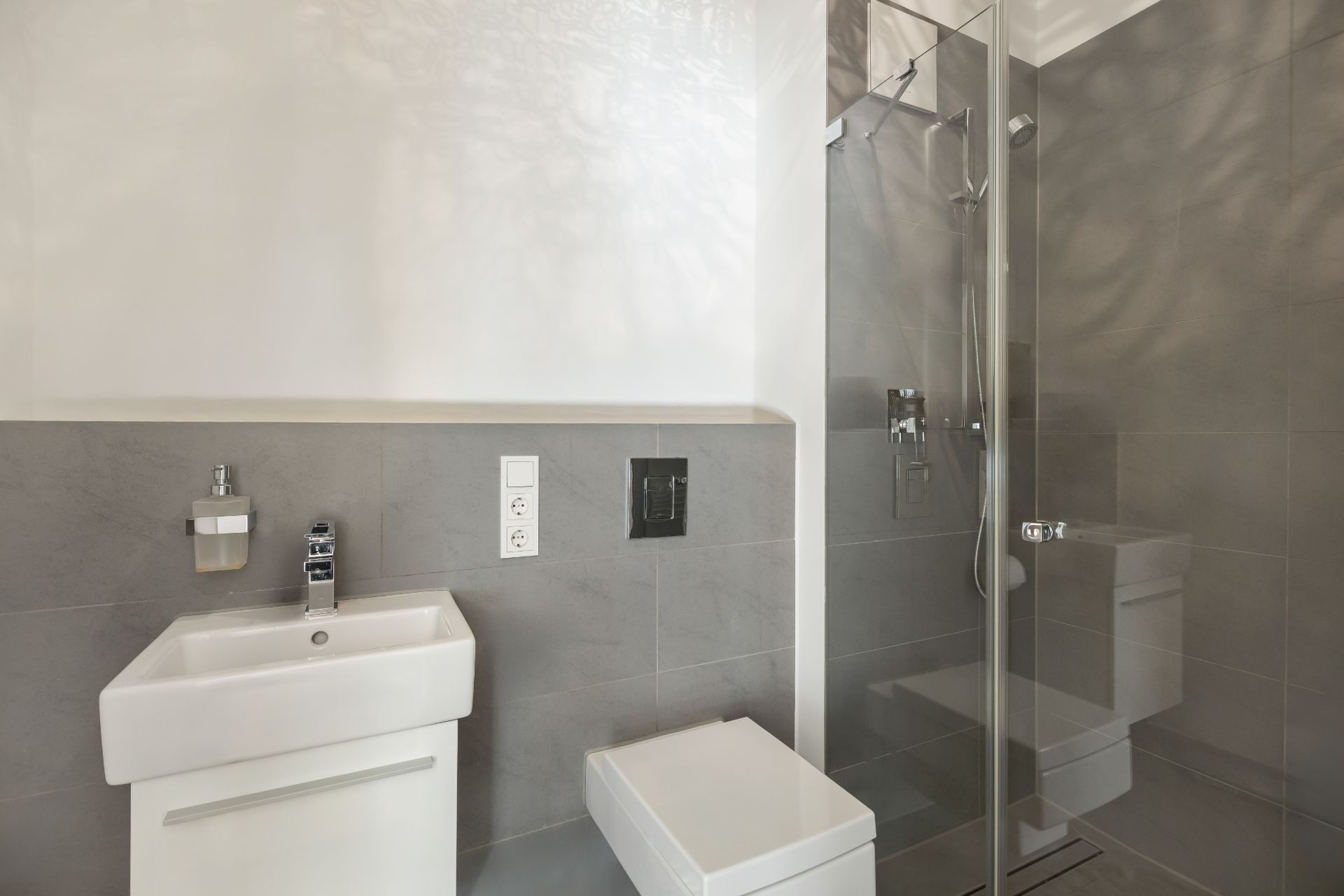 Modernes Badezimmer mit Dusche, Waschbecken und Toilette, graue Fliesen an den Wänden.