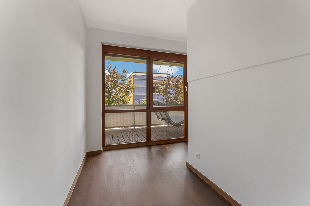 Heller Raum mit Holzboden und großen Fenstern zu einem Balkon.