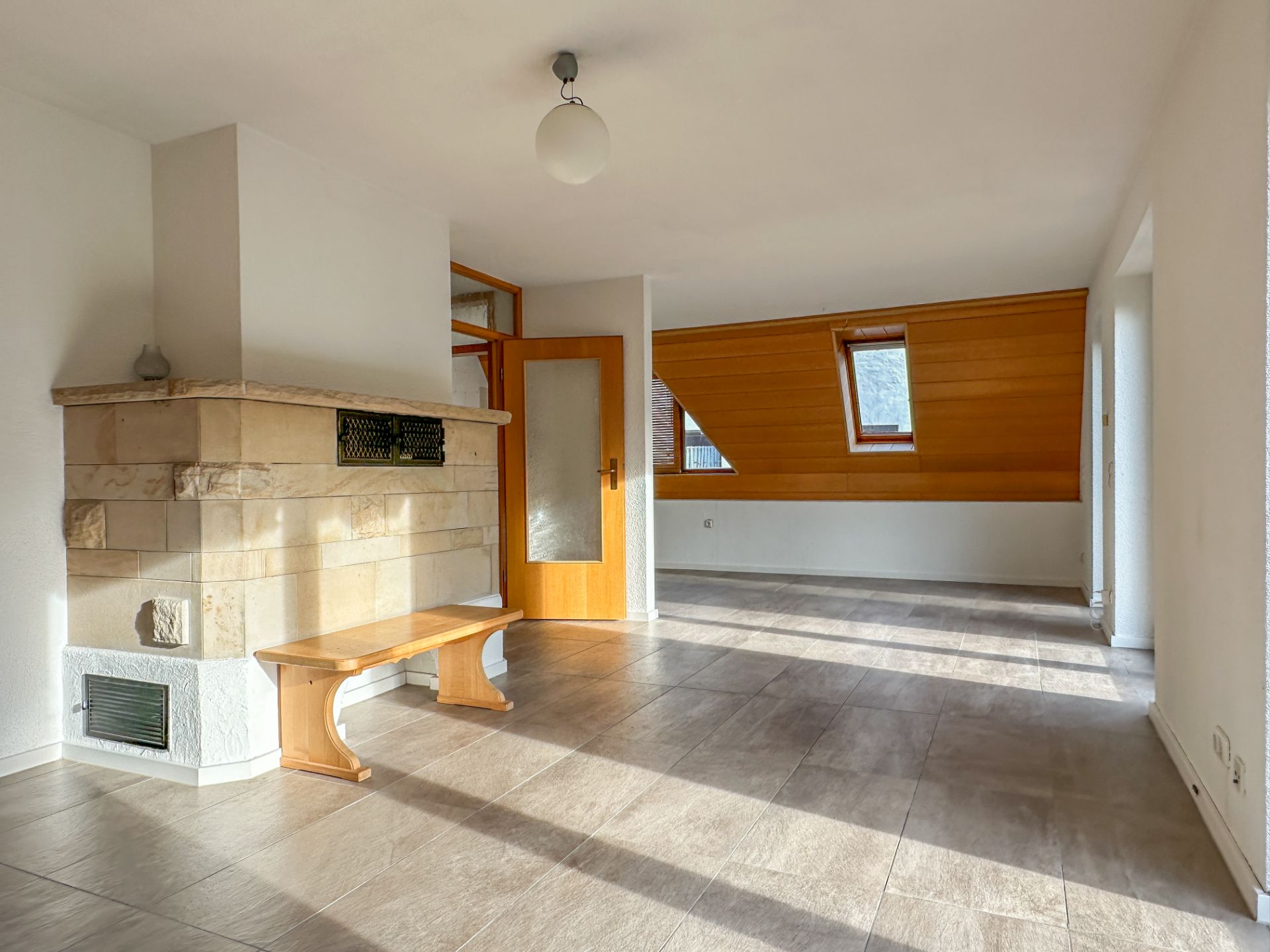 Helles Wohnzimmer mit Kamin, Holztür und Holzverkleidung an der Wand unter einem Fenster.