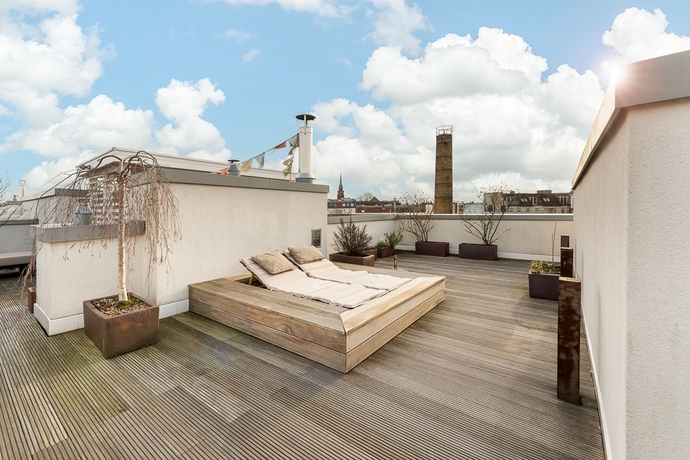 Dachterrasse mit Holzboden, Liegefläche, Pflanzen in Kübeln und Blick auf die Stadt.