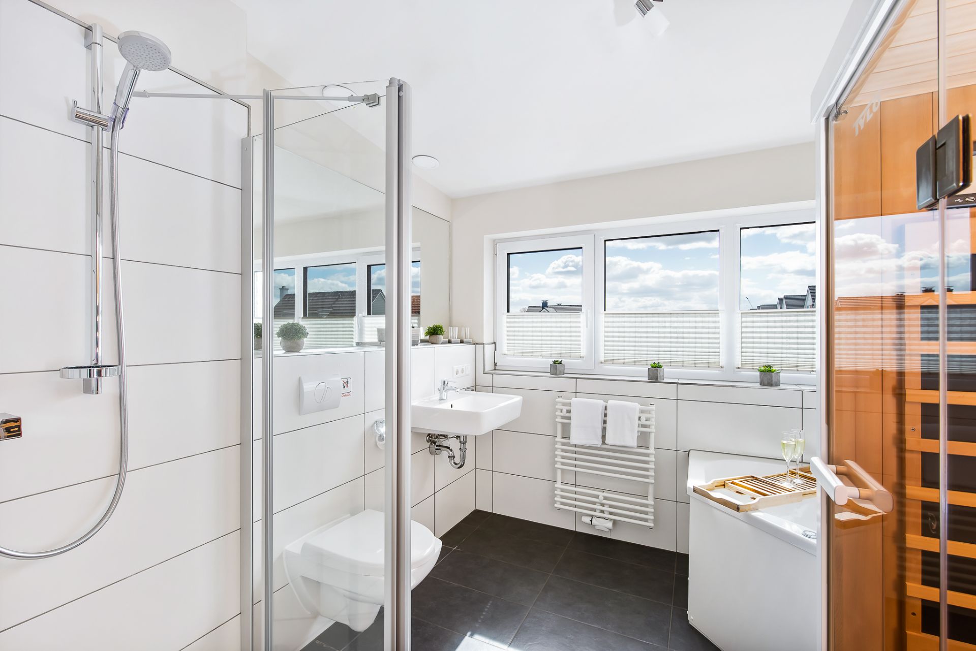 Modernes Badezimmer mit Dusche, WC, Waschbecken, Badewanne und Sauna, große Fenster mit Tageslicht.