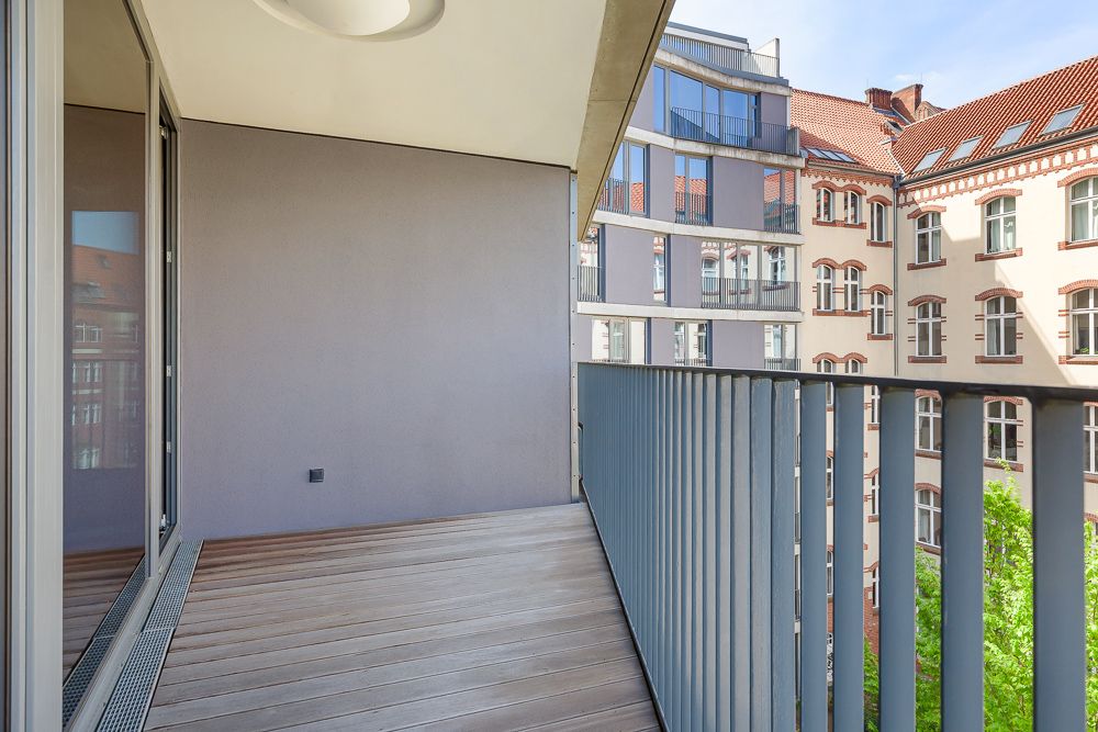 Moderner Balkon mit Holzboden und Metallgeländer, Blick auf Nachbargebäude.