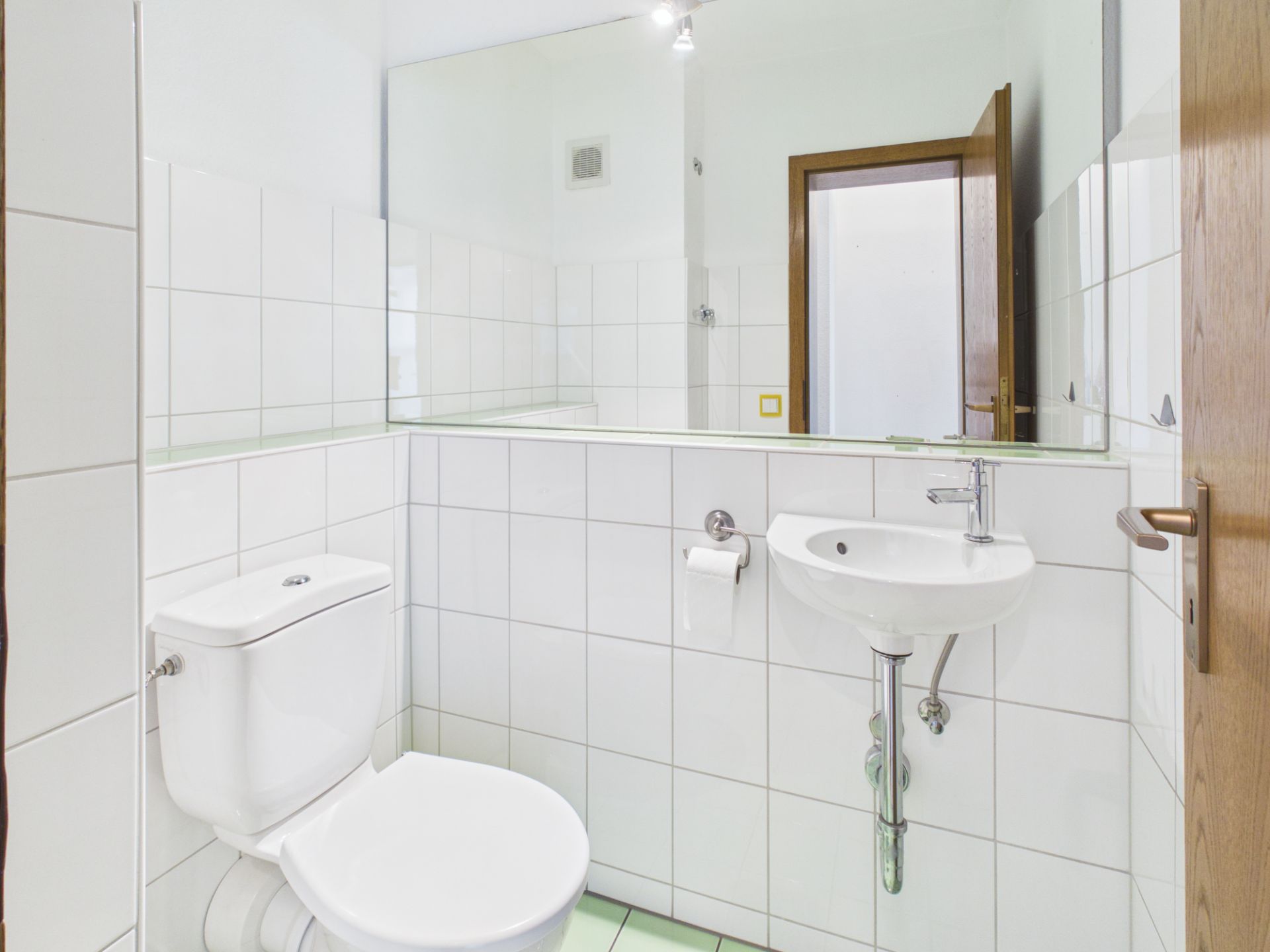 Kleines Badezimmer mit weißer Toilette, Waschbecken und großem Spiegel an der Wand.