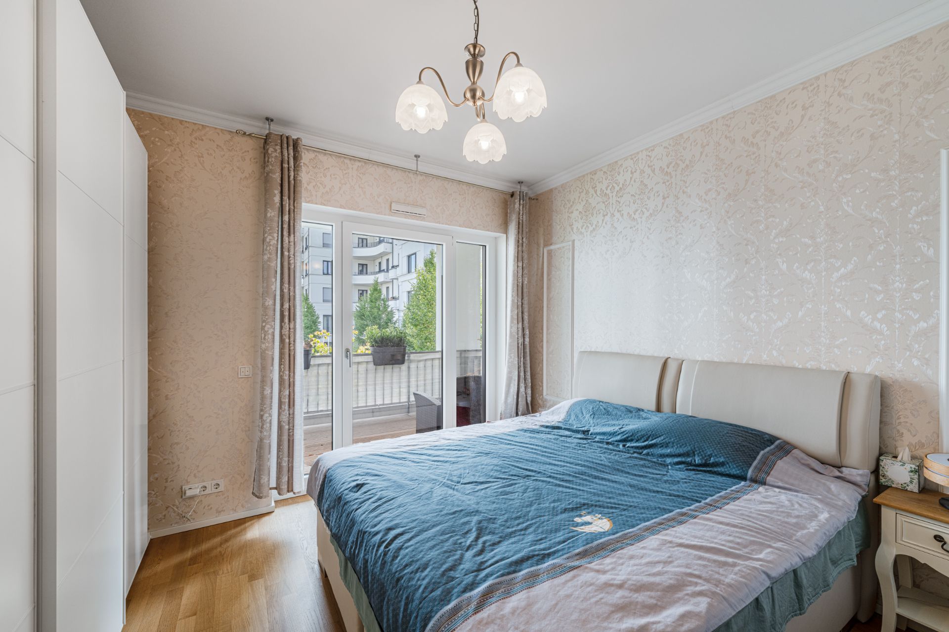 Helles Schlafzimmer mit großem Bett, Kleiderschrank und Zugang zu einem Balkon mit Pflanzen.