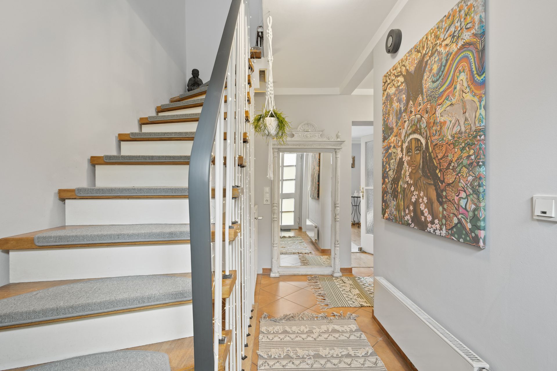 Heller Flur mit Treppe, großem Spiegel, Teppichen und buntem Wandbild.