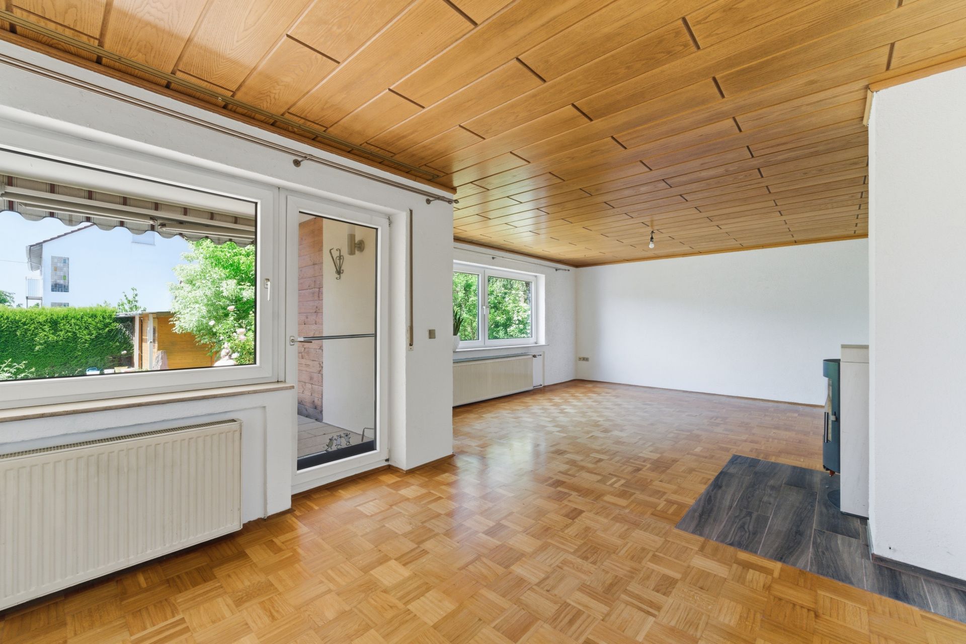 Helles Wohnzimmer mit Parkettboden, Holzdecke, großen Fenstern und Zugang zum Balkon.