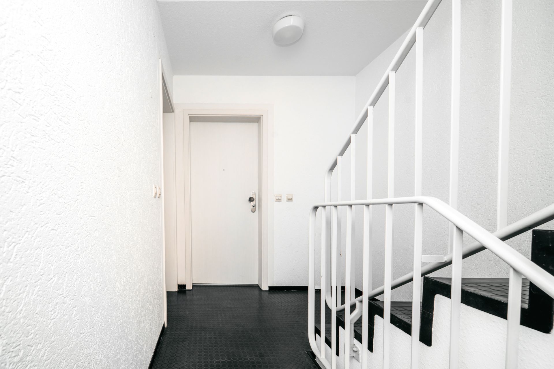 Heller Hausflur mit weißer Wohnungstür und Treppe mit weißem Geländer.
