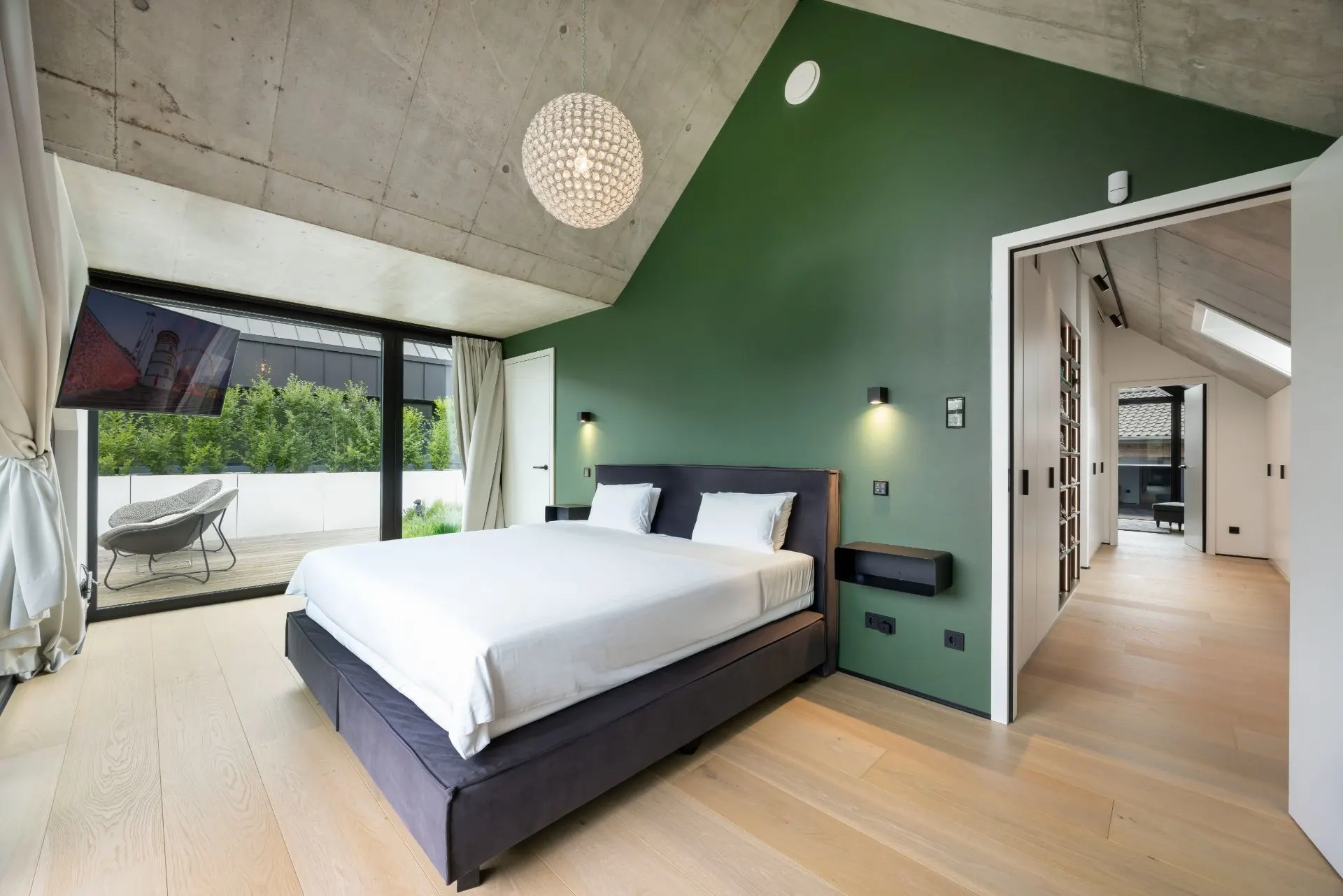Modernes Schlafzimmer mit Doppelbett, grüner Wand, großem Fenster und Zugang zu einer Terrasse.