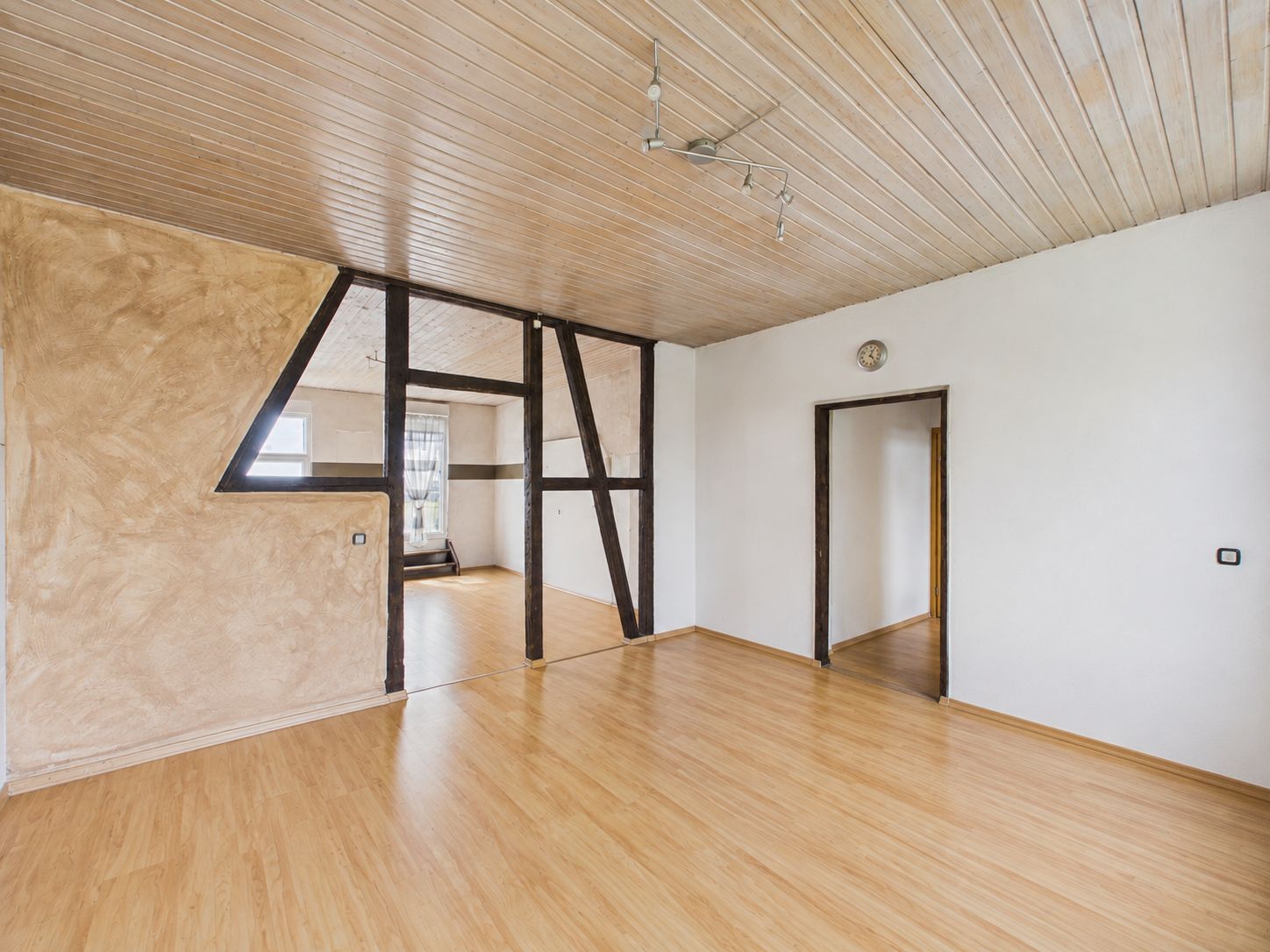 Leerer Raum mit Holzboden, Holzbalken, weißer Wand und Holzdecke.