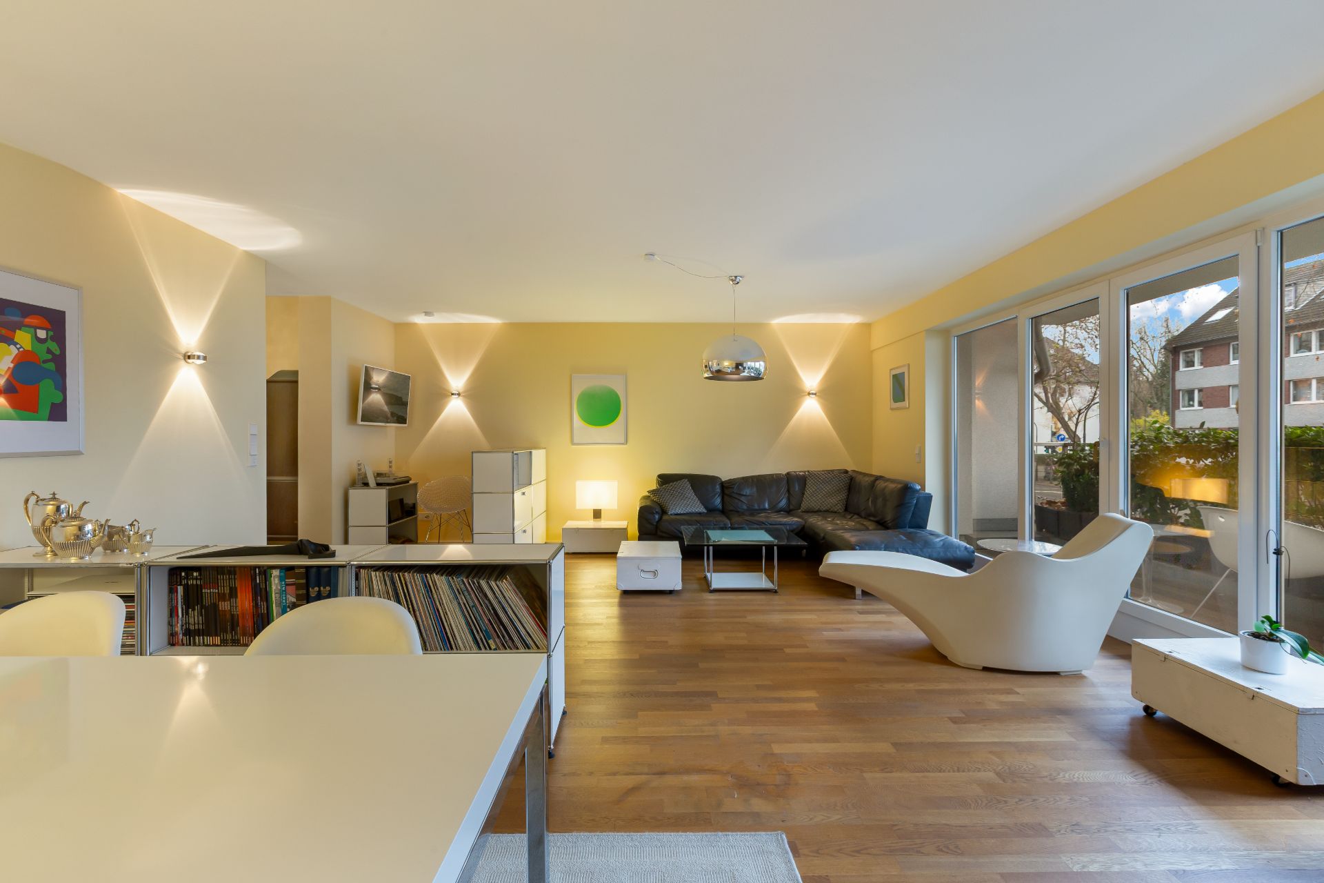 Modernes Wohnzimmer mit Holzfußboden, Ecksofa, Lounge-Stuhl und großen Fenstern zur Terrasse.