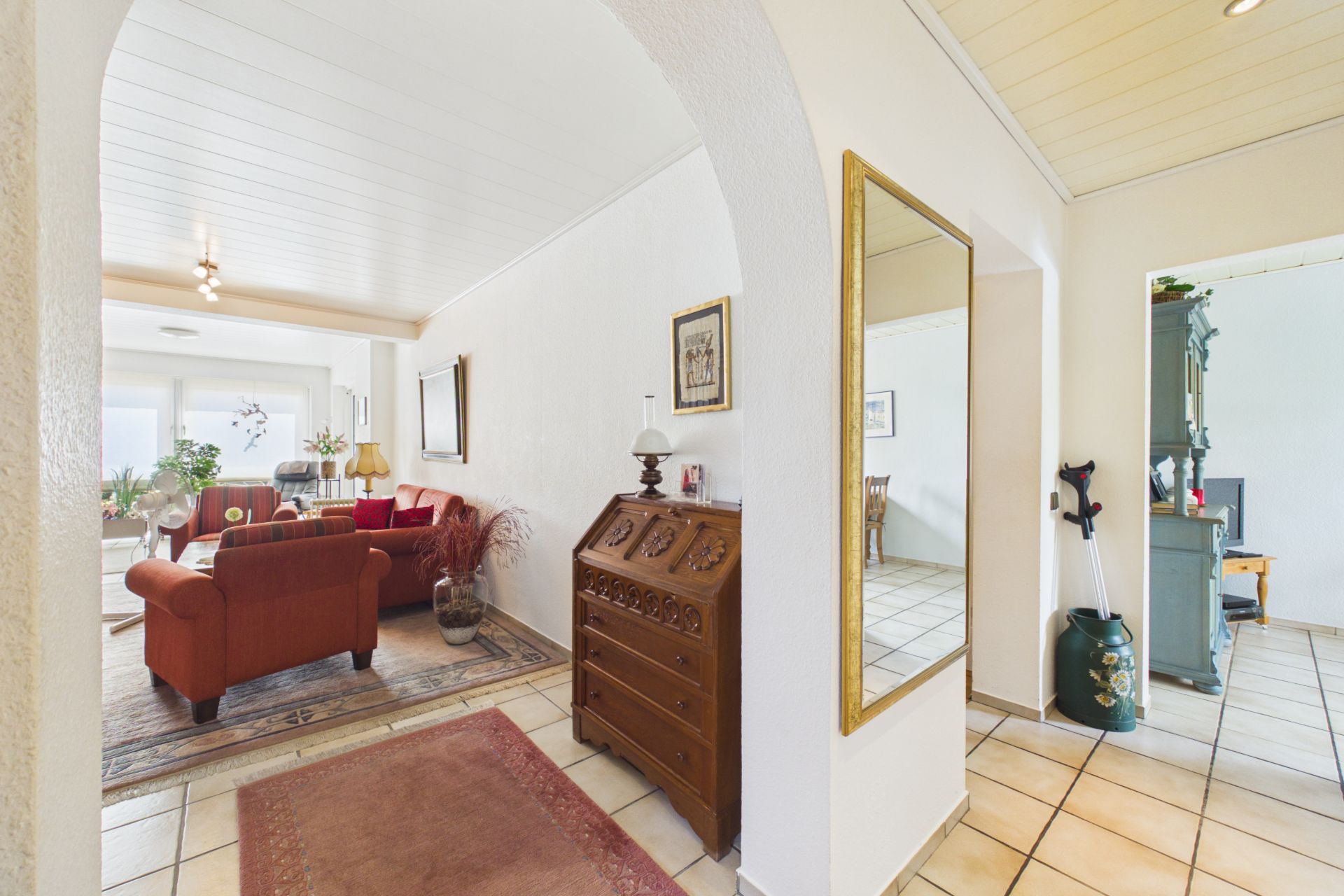 Heller Flur mit Spiegel, Blick ins Wohnzimmer mit roten Sofas und vielen Pflanzen.