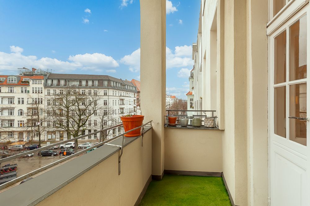 Balkon mit grünem Bodenbelag, Blumentöpfen und Blick auf eine Wohnstraße mit Häusern.