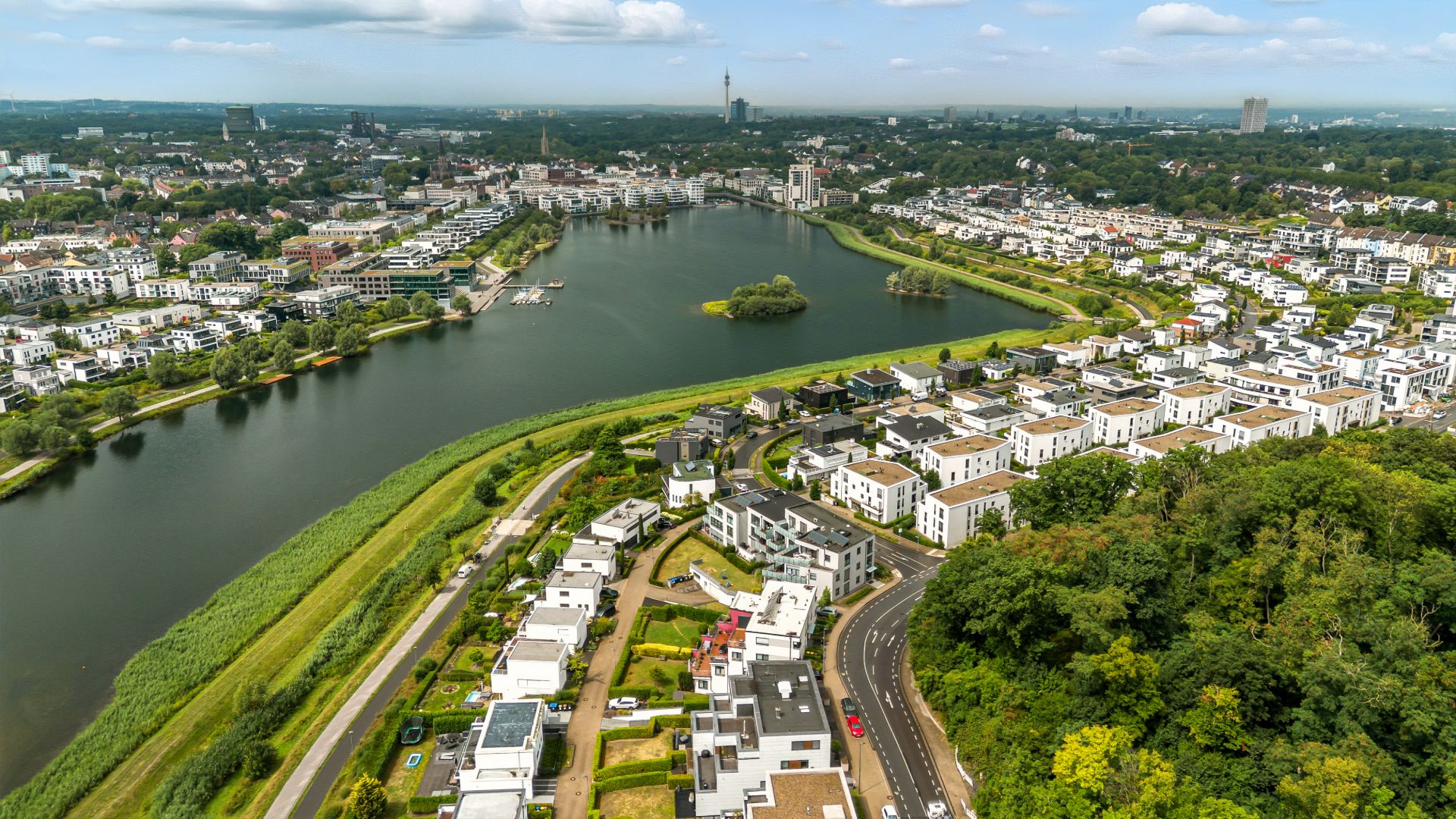 Luftaufnahme eines Wohngebiets mit See, Häusern und viel Grün.