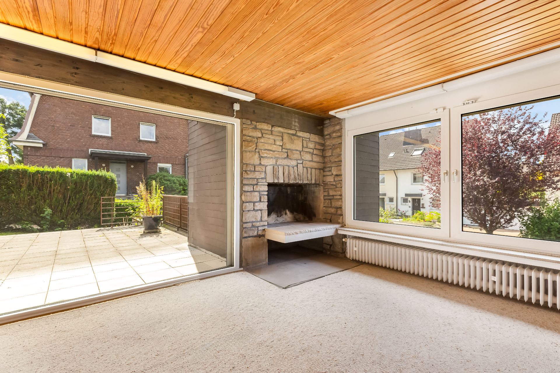 Helles Zimmer mit Kamin, großen Fenstern und Blick auf Terrasse und Garten.