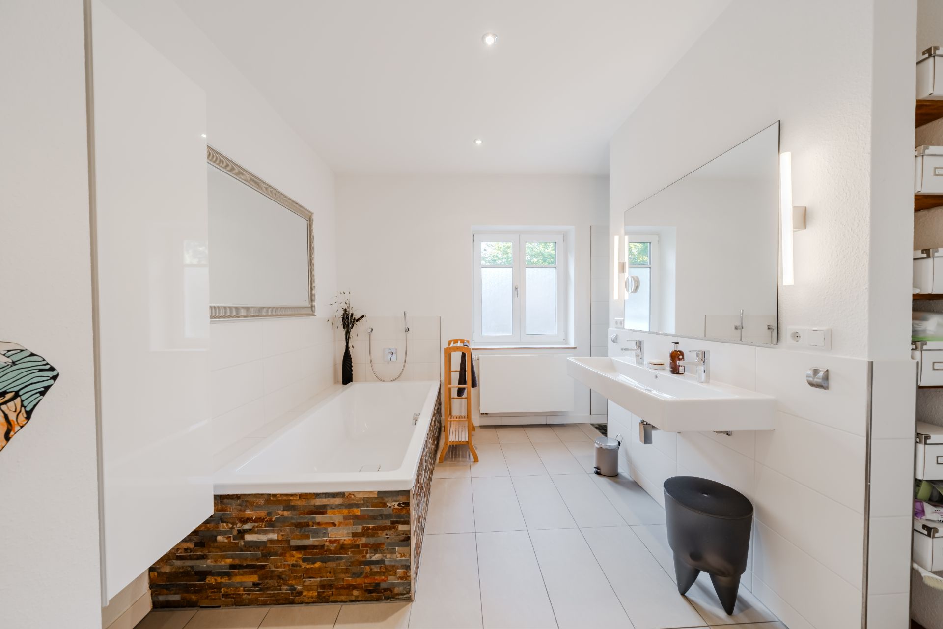 Modernes, helles Badezimmer mit Badewanne, großem Spiegel und Fenster.