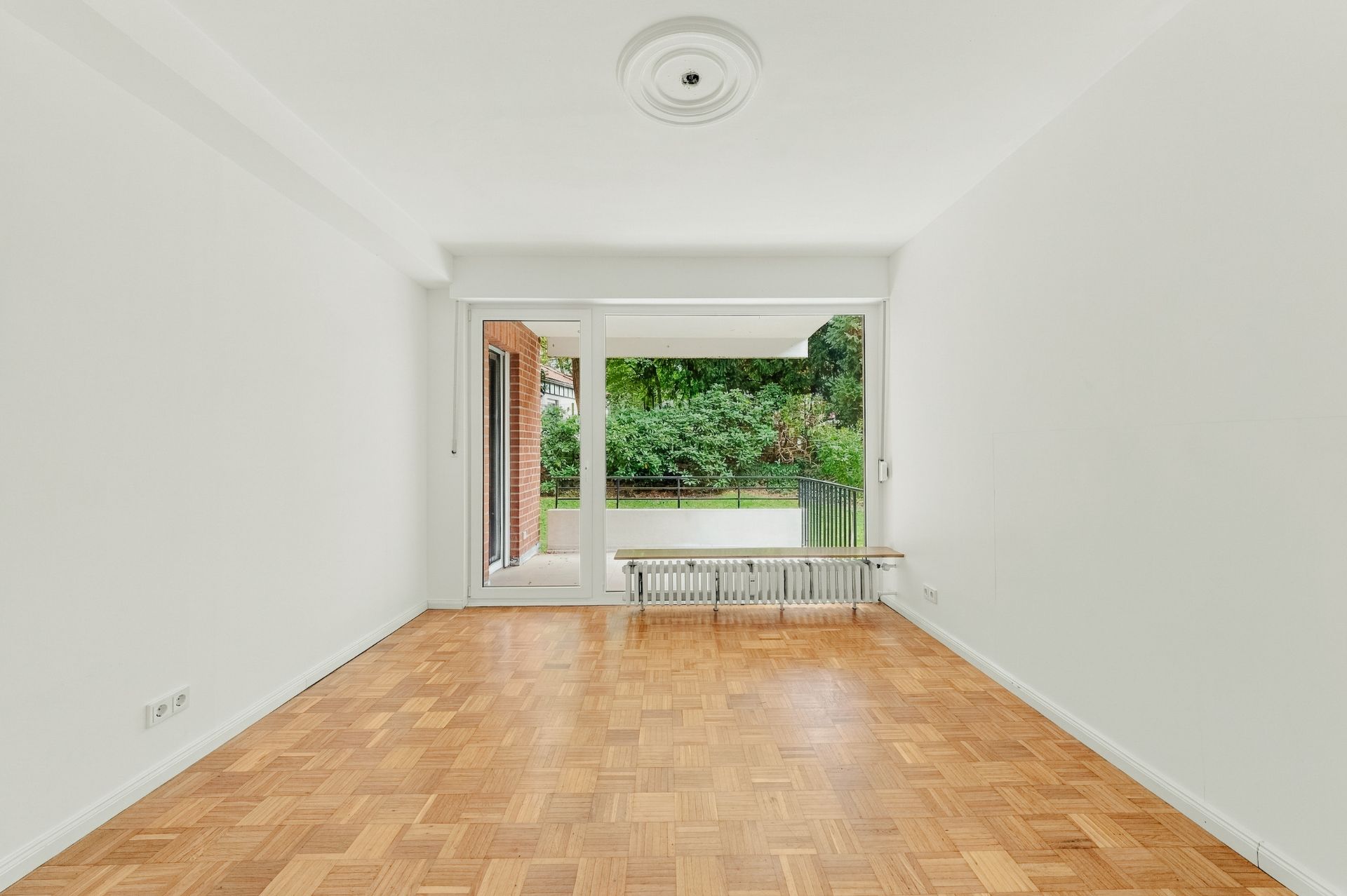 Helles Wohnzimmer mit Parkettboden und großen Fenstern, Blick auf einen grünen Garten.
