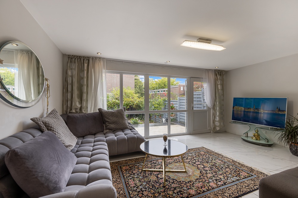 Helles Wohnzimmer mit grauem Sofa, Teppich, Glastisch und großem Fenster zur Terrasse.