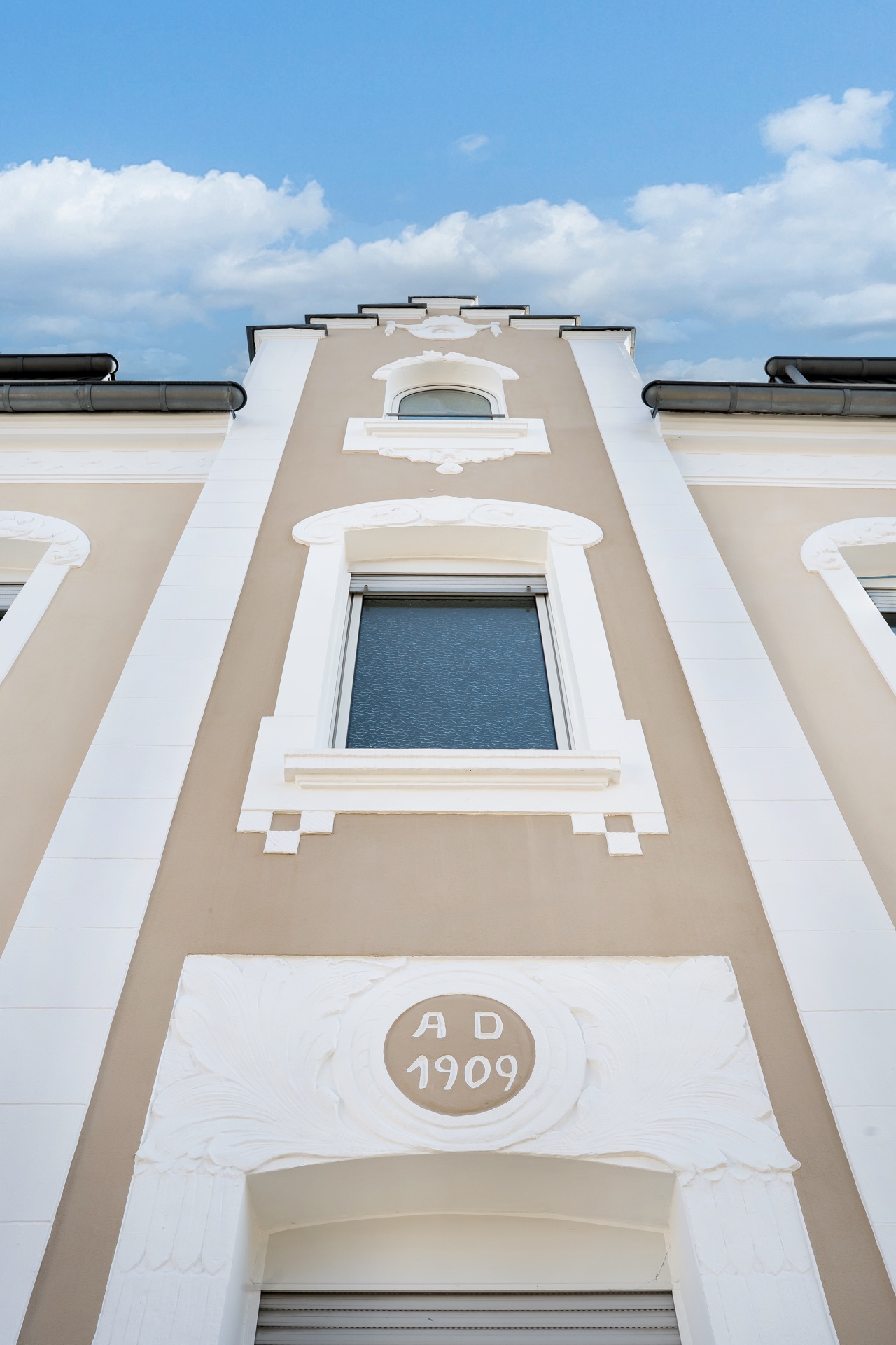 Fassade eines Wohnhauses mit Zierfenstern und der Jahreszahl 1909 über dem Eingang.