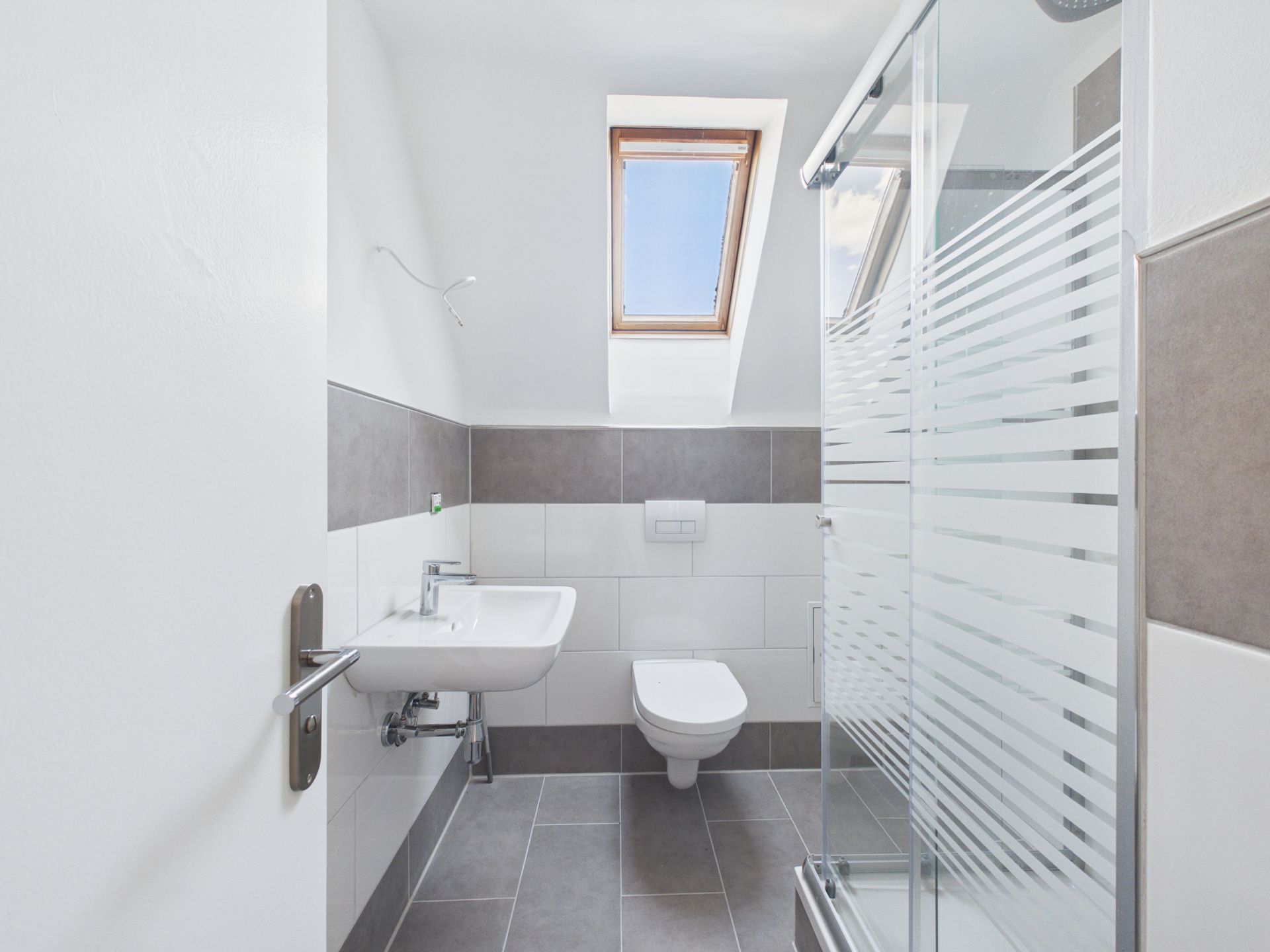 Helles Badezimmer mit Waschbecken, Toilette, Dusche und Dachfenster.