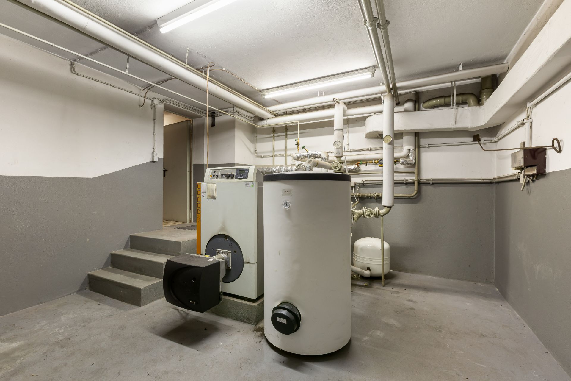 Heizungsraum mit Kessel, Warmwasserspeicher und sichtbaren Rohrleitungen.