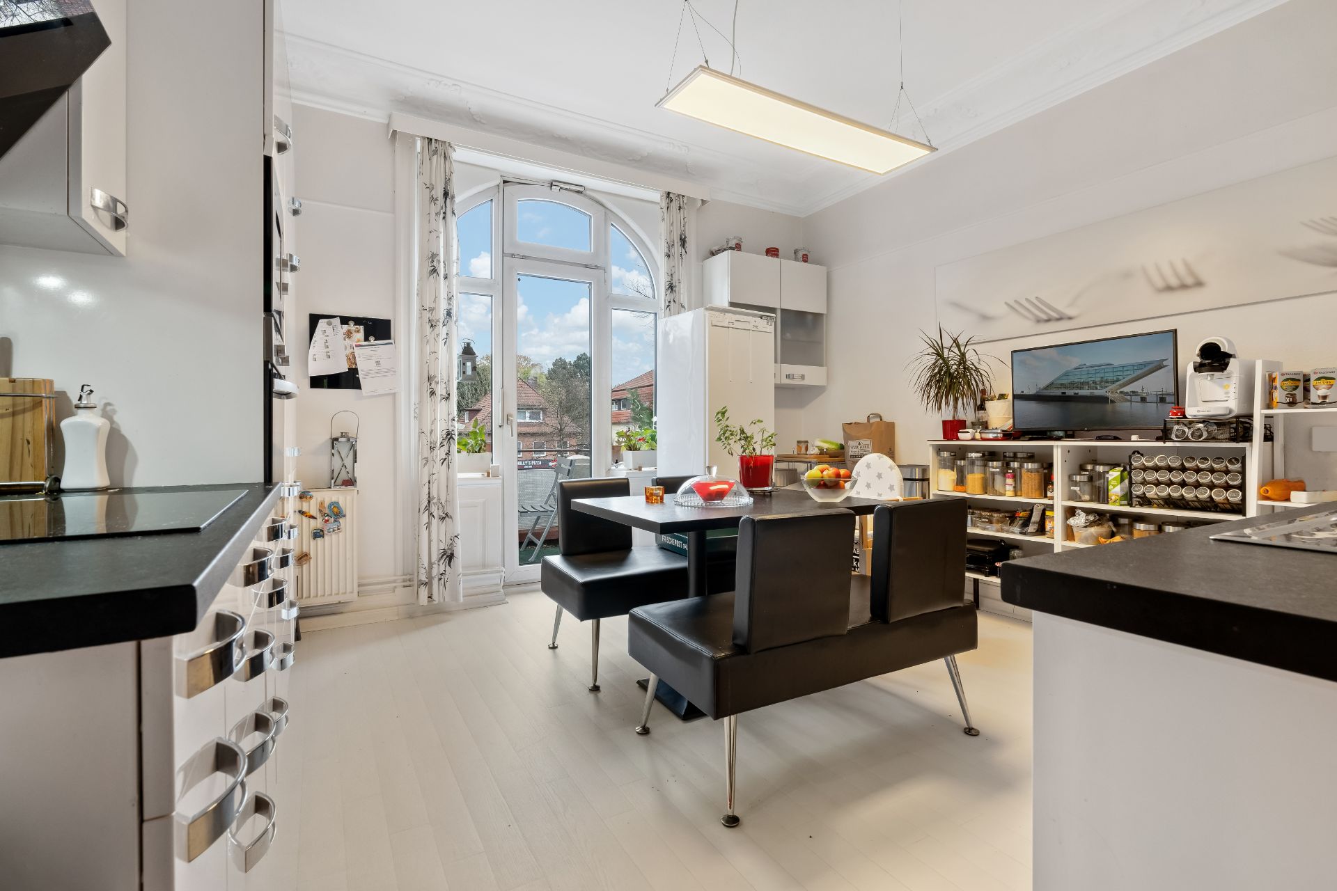 Moderne Küche mit Esstisch, Stühlen, Balkonzugang und Regalen mit Gewürzen und Fernseher.