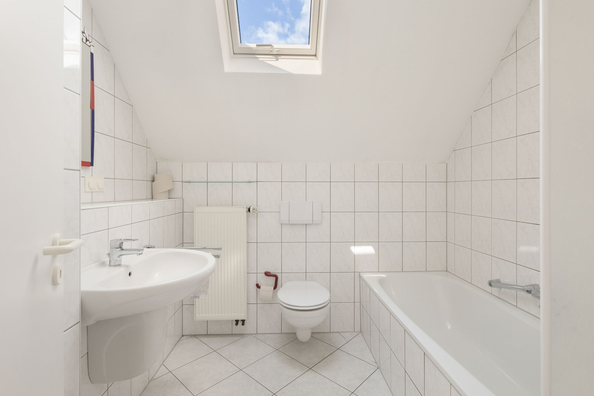 Helles Badezimmer mit Dachfenster, Badewanne, Waschbecken, WC und weißen Fliesen.