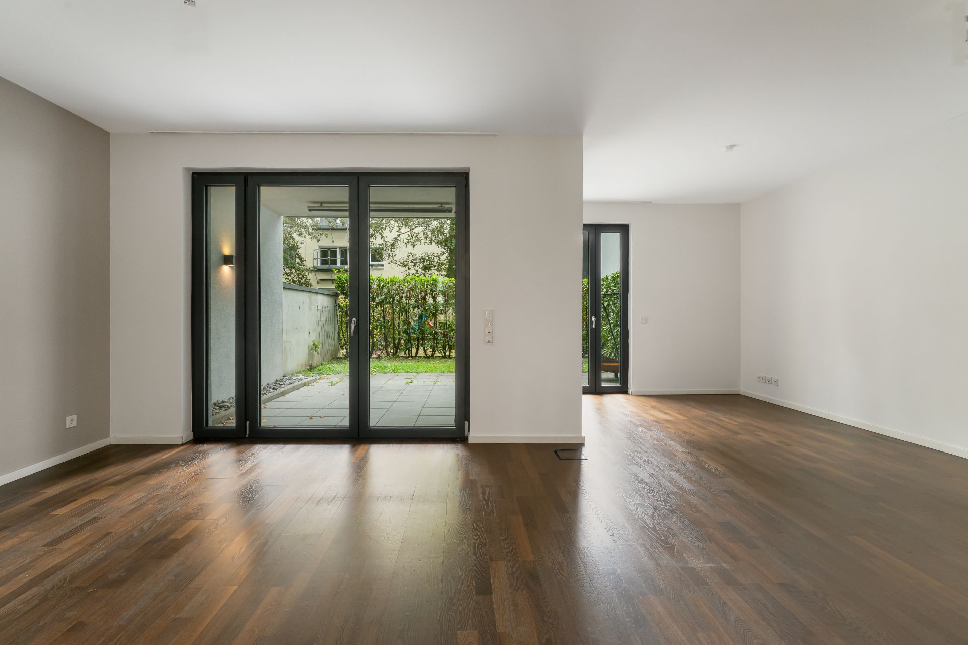 Heller Wohnraum mit Parkettboden, großen Fenstern und Zugang zur Terrasse mit Garten.