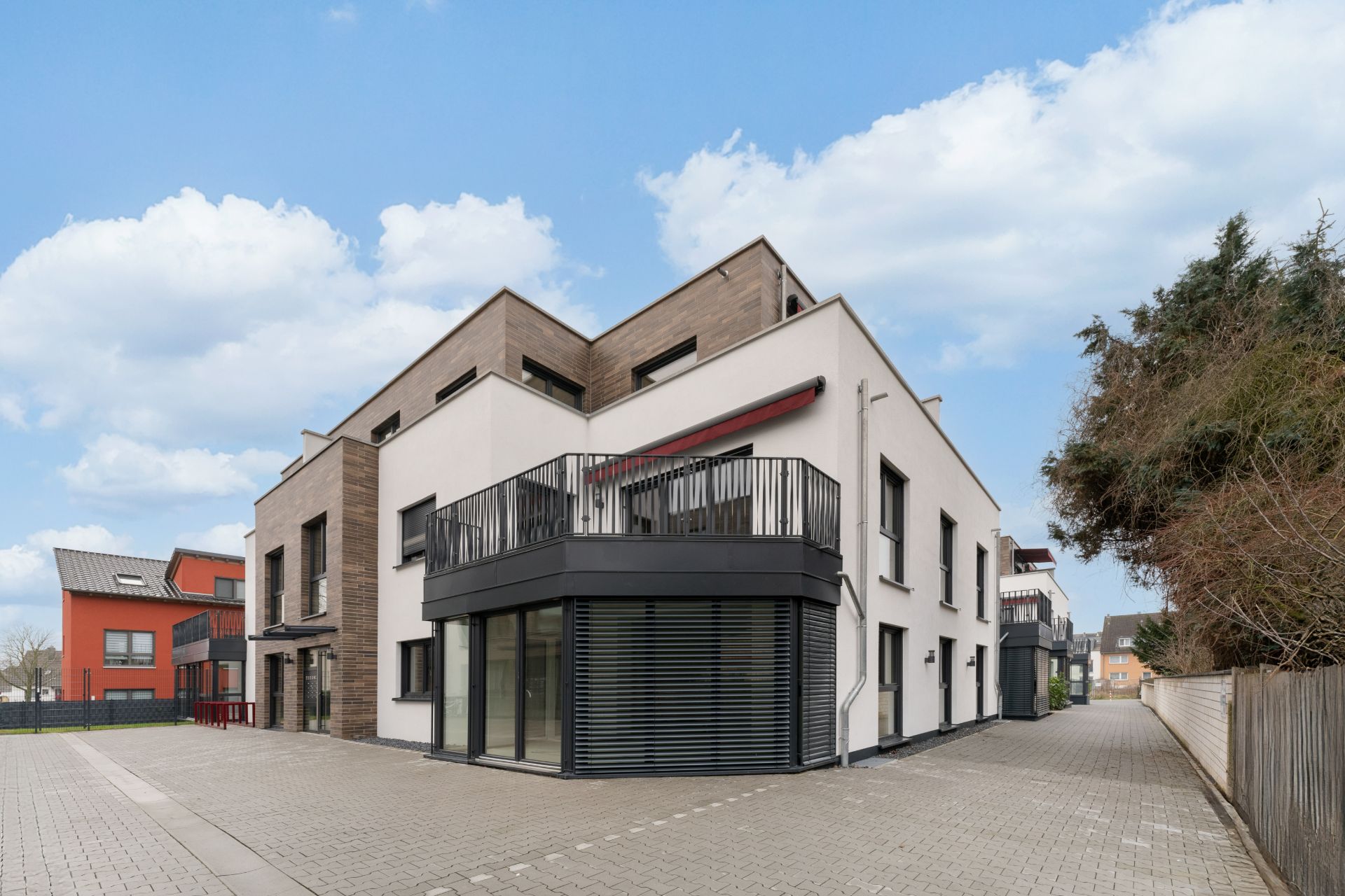 Modernes Wohngebäude mit großem Balkon und Glasfront, daneben gepflasterter Weg.