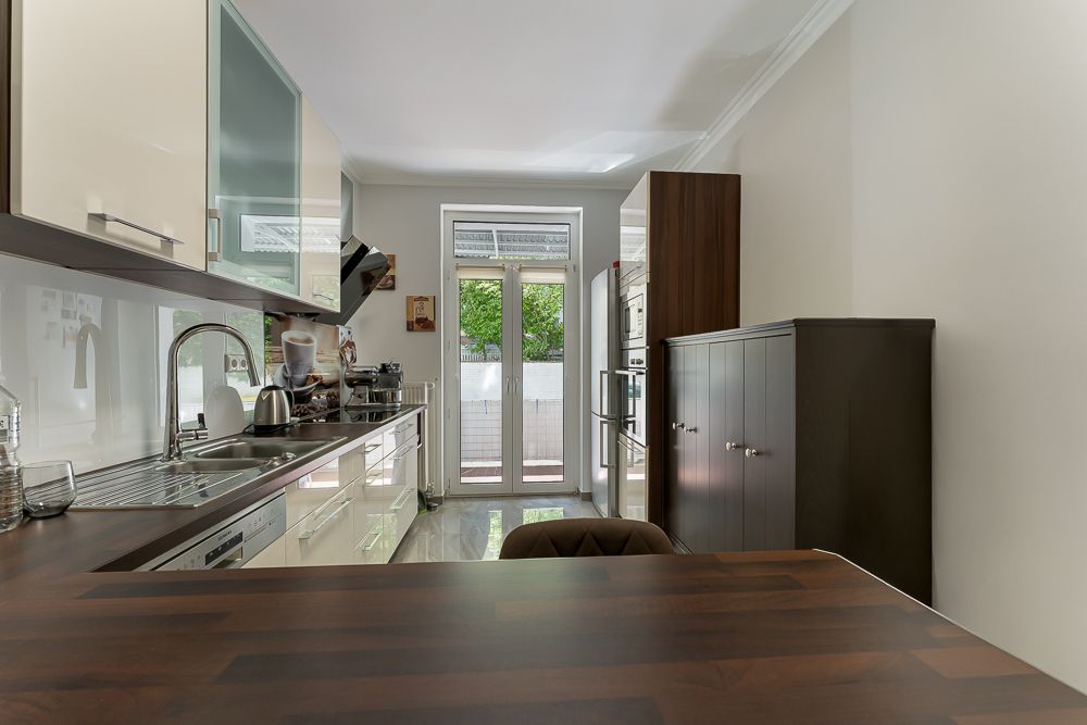 Moderne Küche mit Holzarbeitsplatte, weißen Schränken und Zugang zu einem Balkon oder Terrasse.