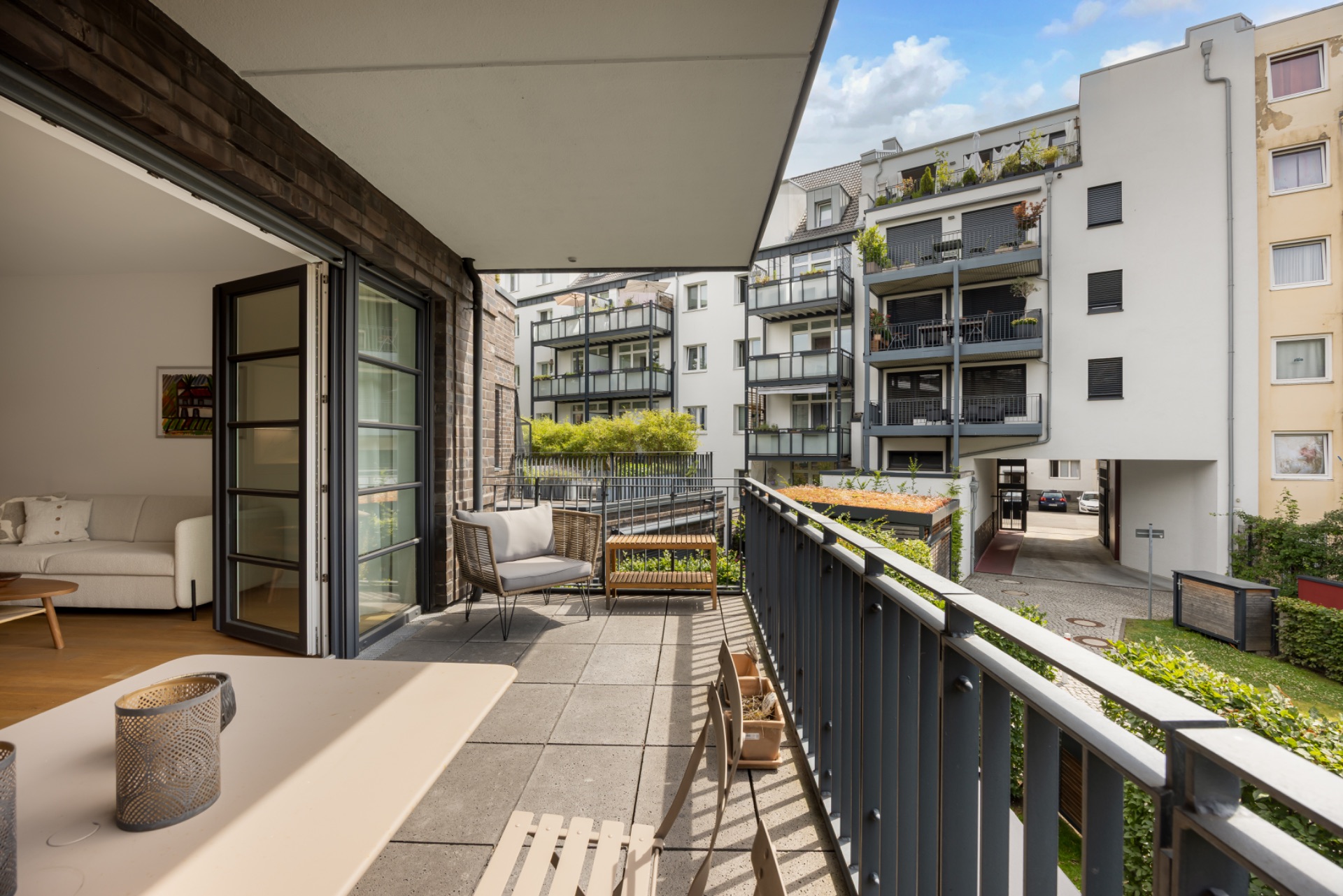 Balkon mit Tisch und Stühlen, Blick auf Innenhof und moderne Wohngebäude.