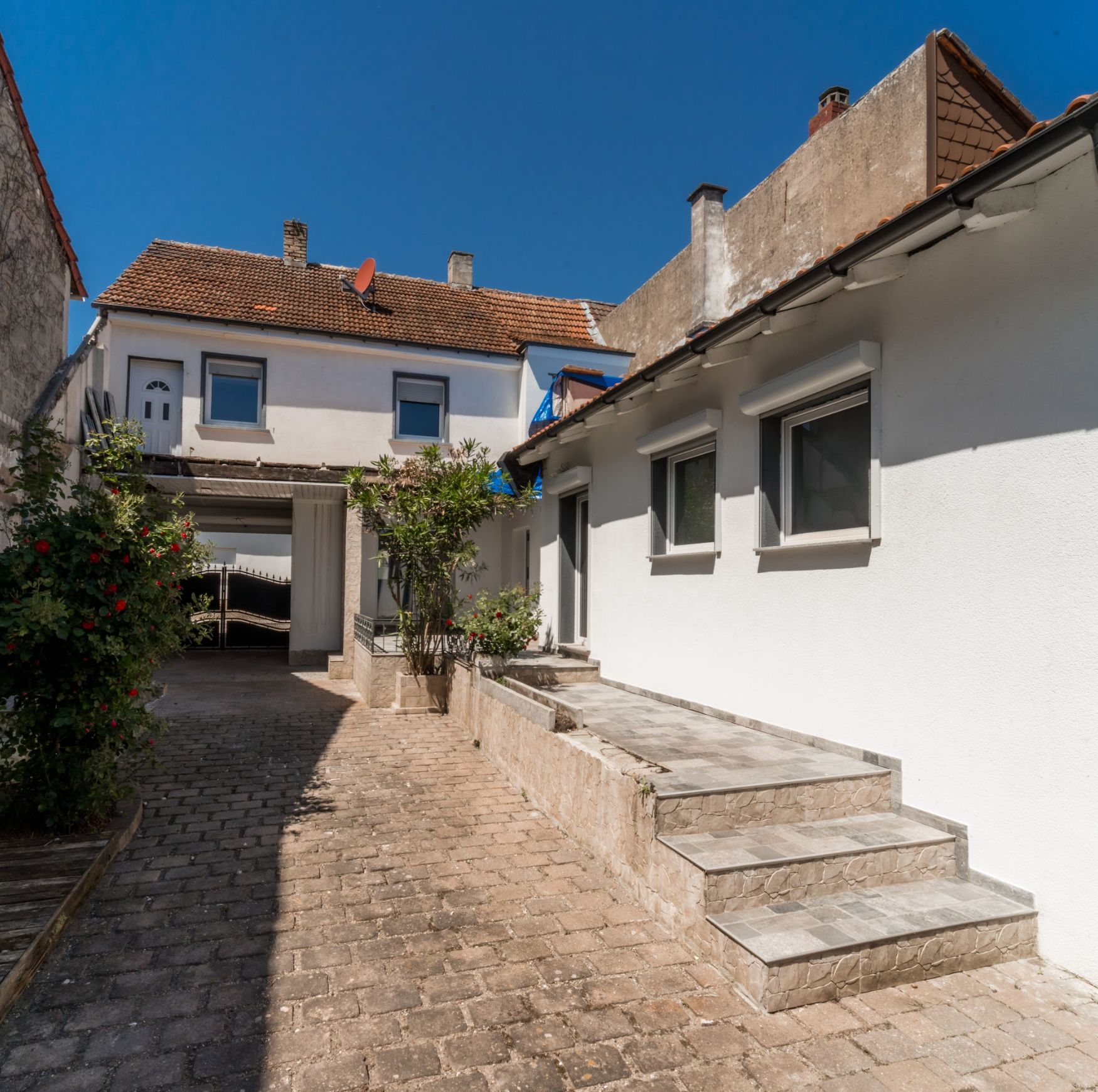 Gepflasterter Innenhof mit Treppe, weißen Wänden und einigen Pflanzen neben Wohngebäuden.