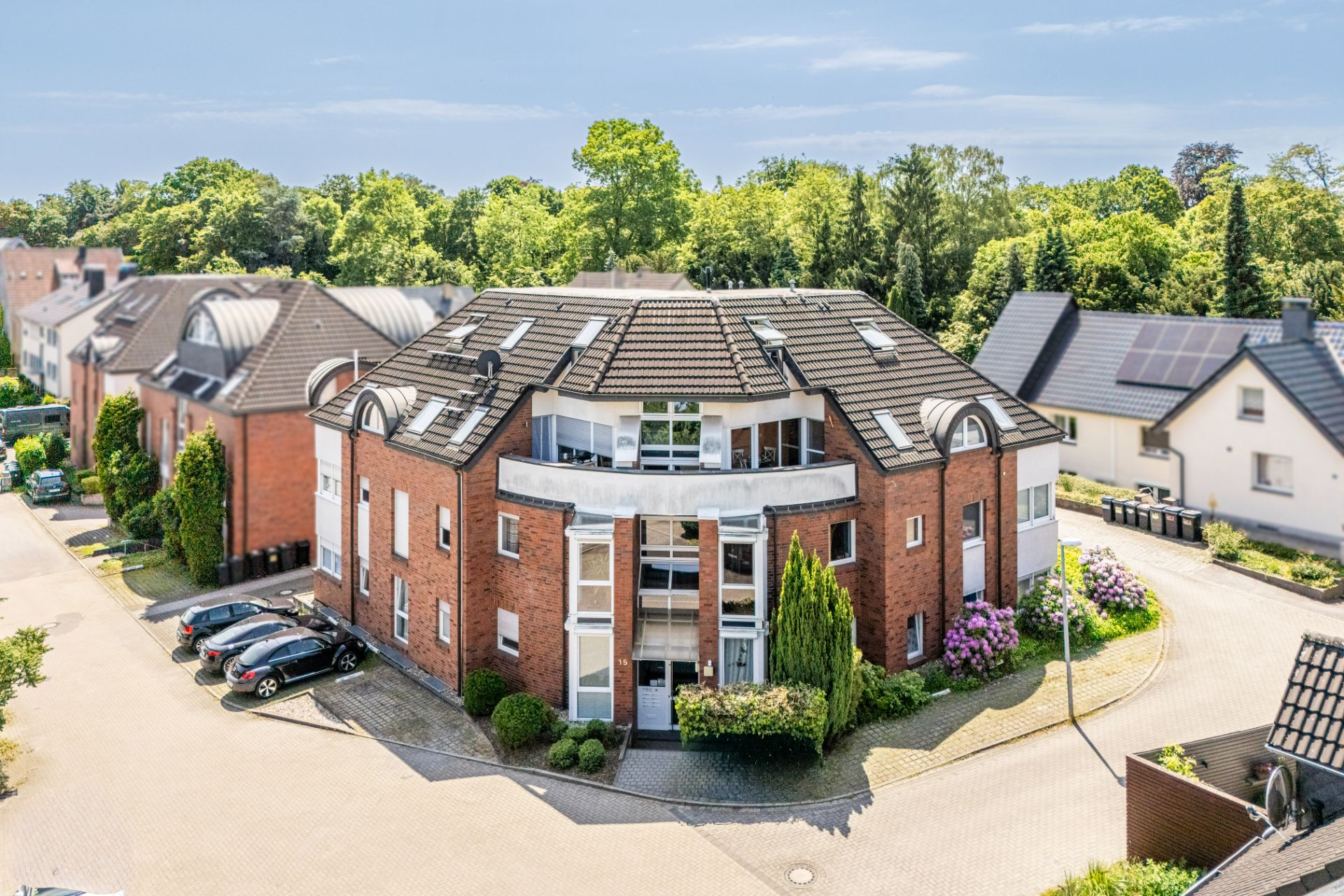 Mehrfamilienhaus aus rotem Backstein mit Balkonen und umgebender Bepflanzung an einer Wohnstraße.