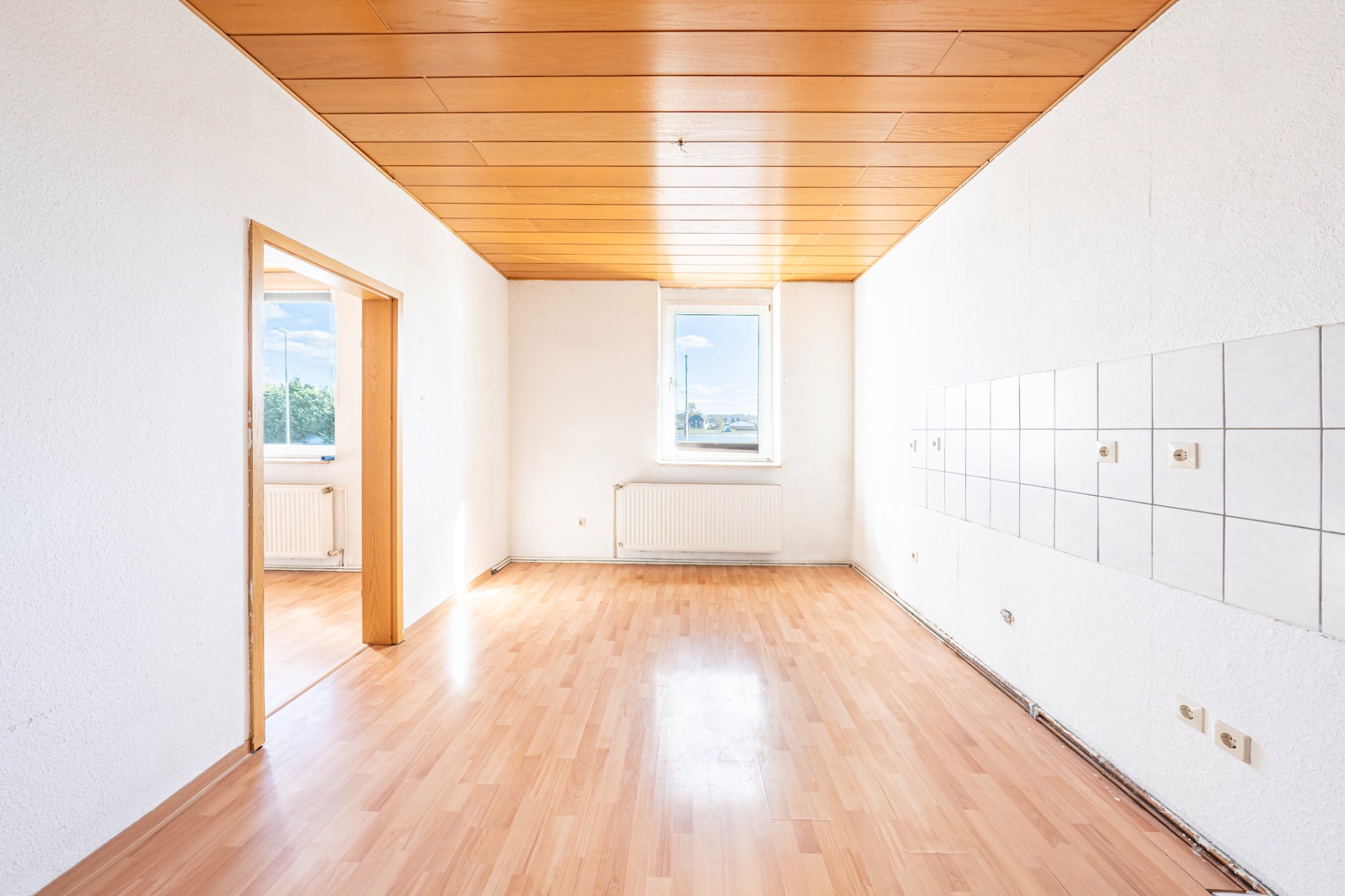 Heller leerer Raum mit Holzboden, Holzdecke und weißen Fliesen an einer Wand.