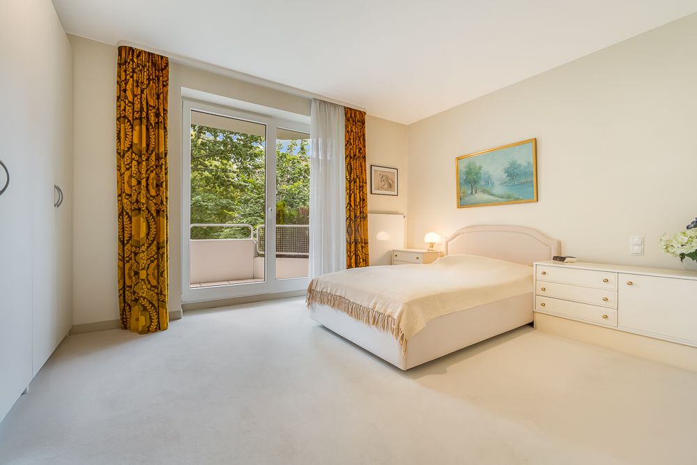 Helles Schlafzimmer mit Doppelbett, weißen Möbeln, goldenen Vorhängen und Zugang zu einem Balkon.