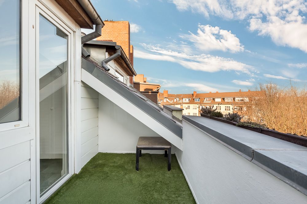 Kleine Dachterrasse mit Kunstrasen und einem kleinen Tisch, Blick auf Nachbarhäuser.