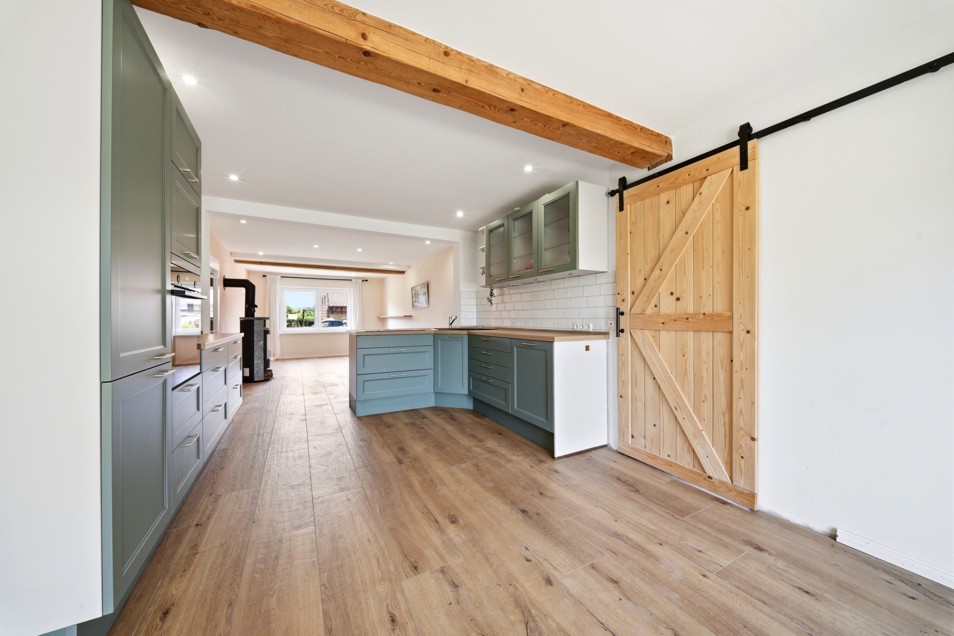 Helle Küche mit Holzfußboden, grünen Schränken und einer Schiebetür aus Holz.