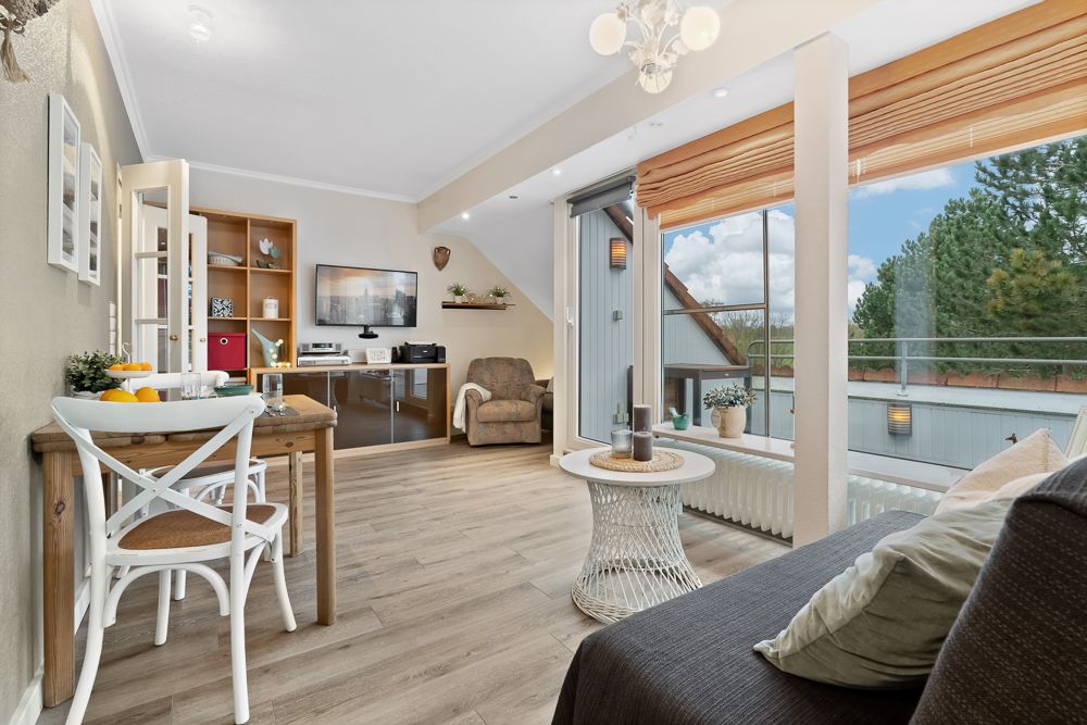 Helles Wohnzimmer mit Esstisch, Sofa, Sessel, Schreibtisch und großen Fenstern mit Blick nach draußen.