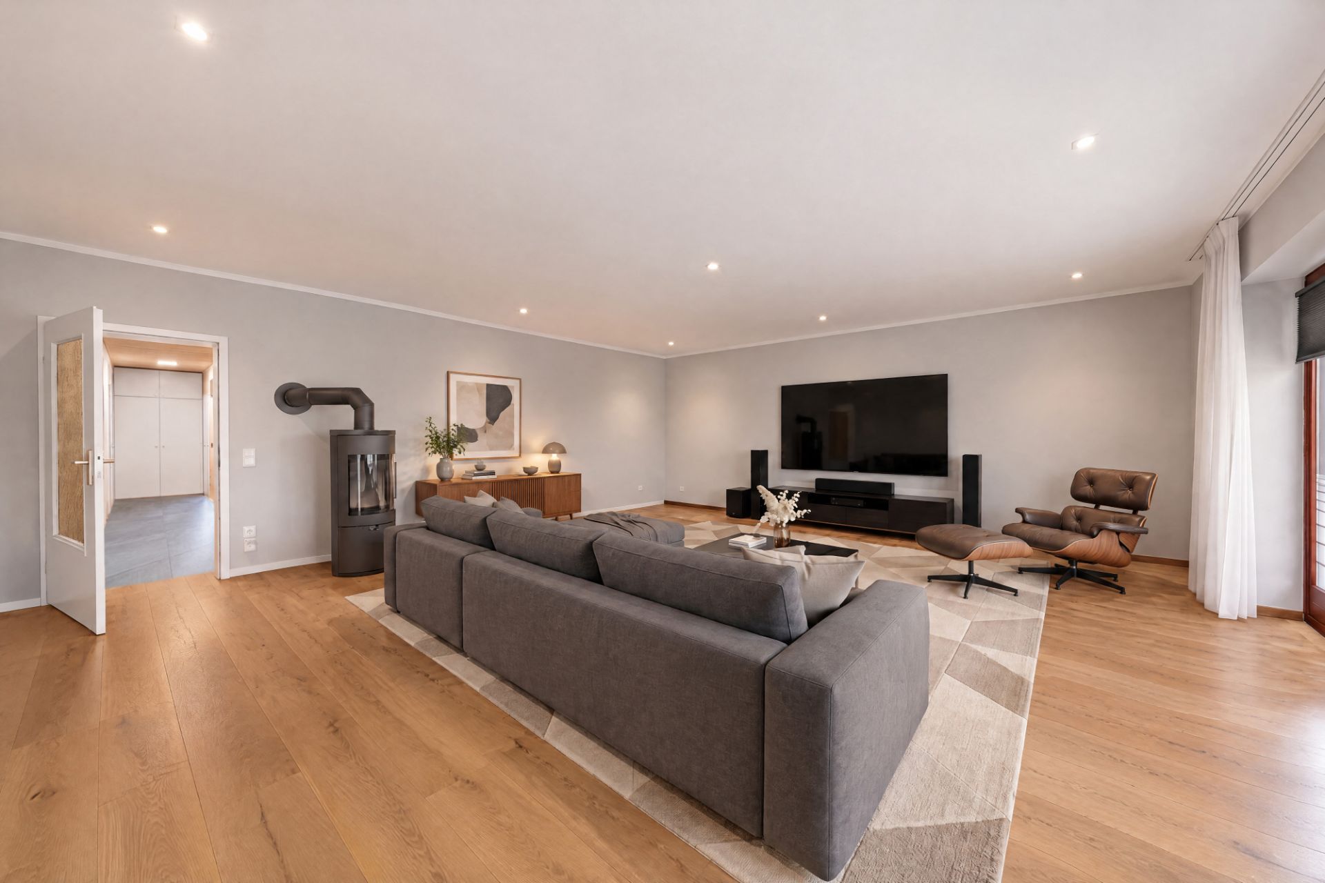 Modernes Wohnzimmer mit grauem Sofa, Holzfußboden, Fernseher, Sessel und großem Teppich.