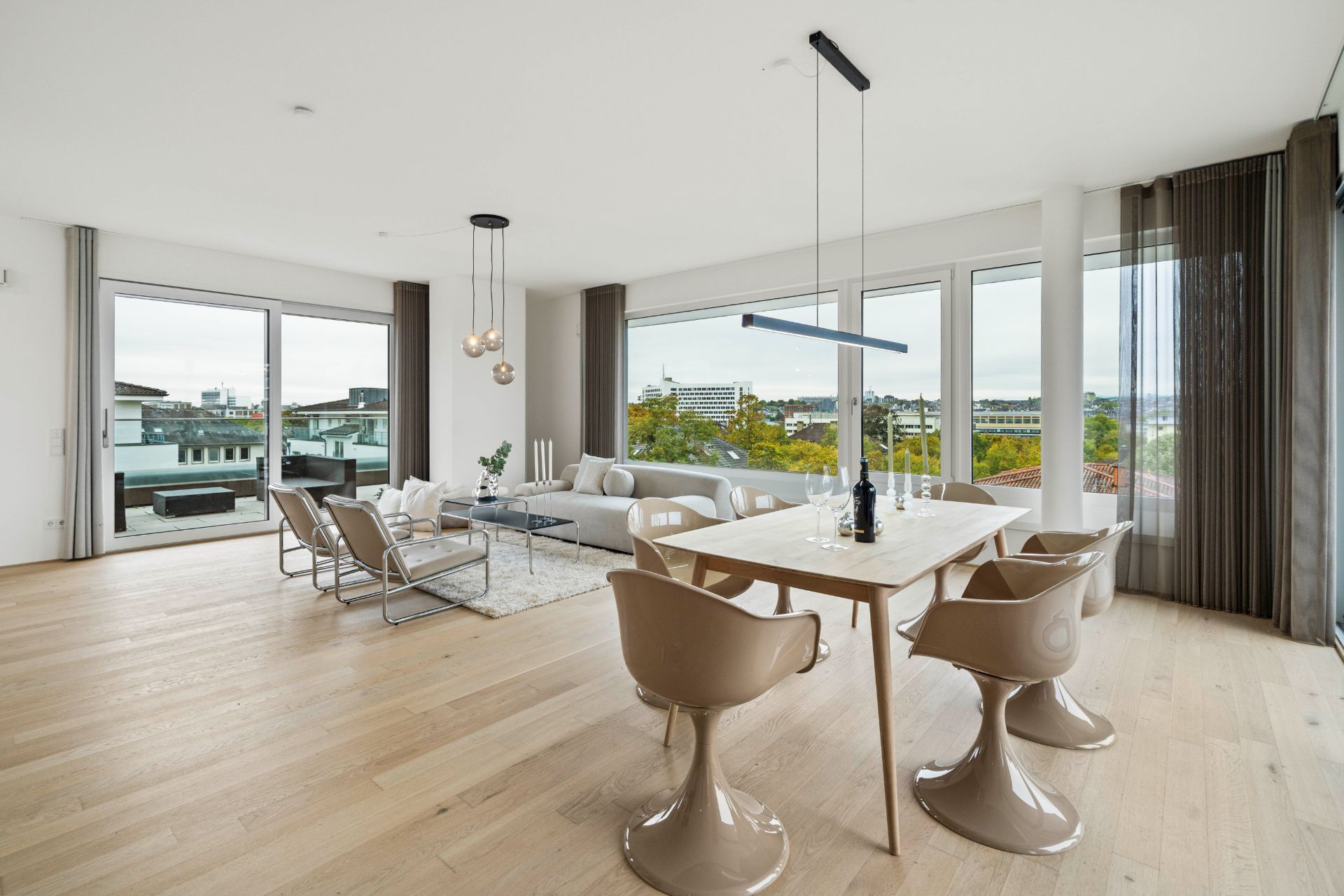 Helles Wohnzimmer mit Essbereich, modernen Stühlen, Sofa und großen Fenstern mit Stadtblick.