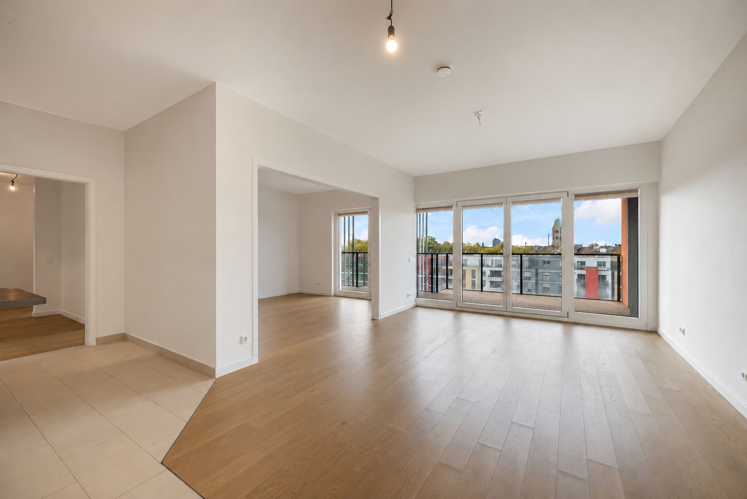 Helles Wohnzimmer mit großen Fenstern, Holzboden und Zugang zu einem Balkon.