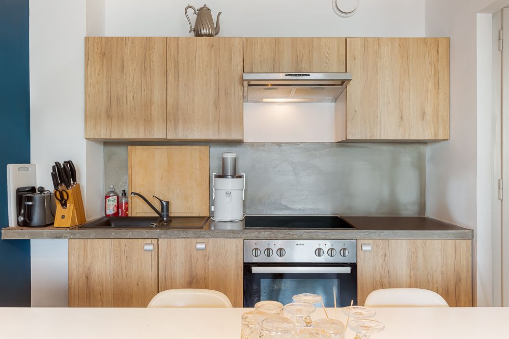 Moderne Küche mit Holzschränken, Herd, Spüle und Küchengeräten auf der Arbeitsplatte.