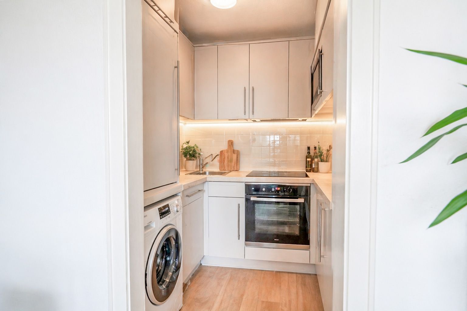 Moderne kleine Küche mit weißen Schränken, Backofen, Waschmaschine und Holzfußboden.