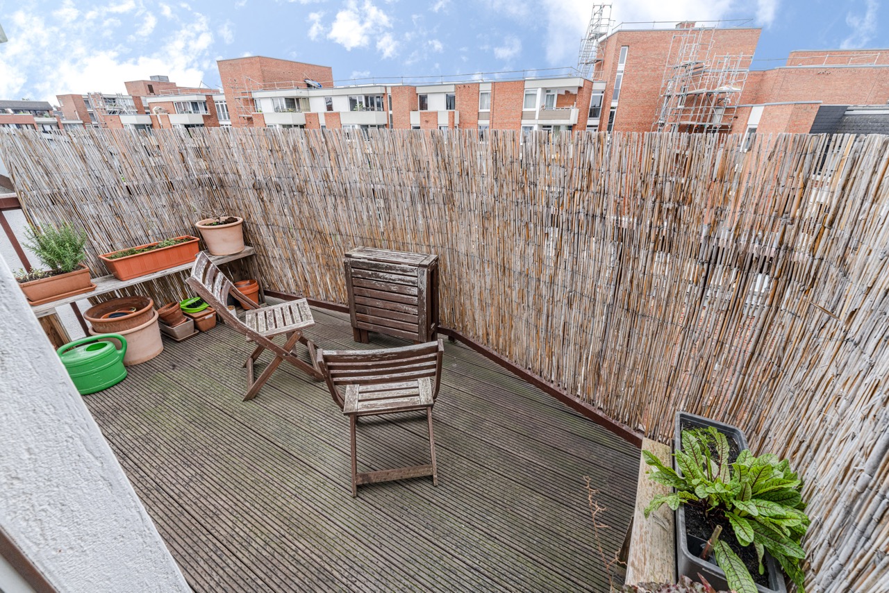 Kleine Holzterrasse mit zwei Stühlen, Blumentöpfen und Bambus-Sichtschutz.