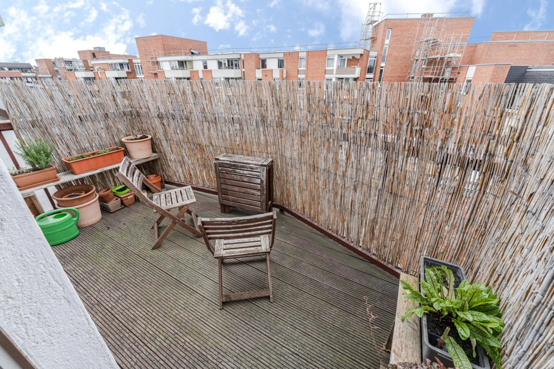 Kleine Holzterrasse mit zwei Stühlen, Blumentöpfen und Bambus-Sichtschutz.
