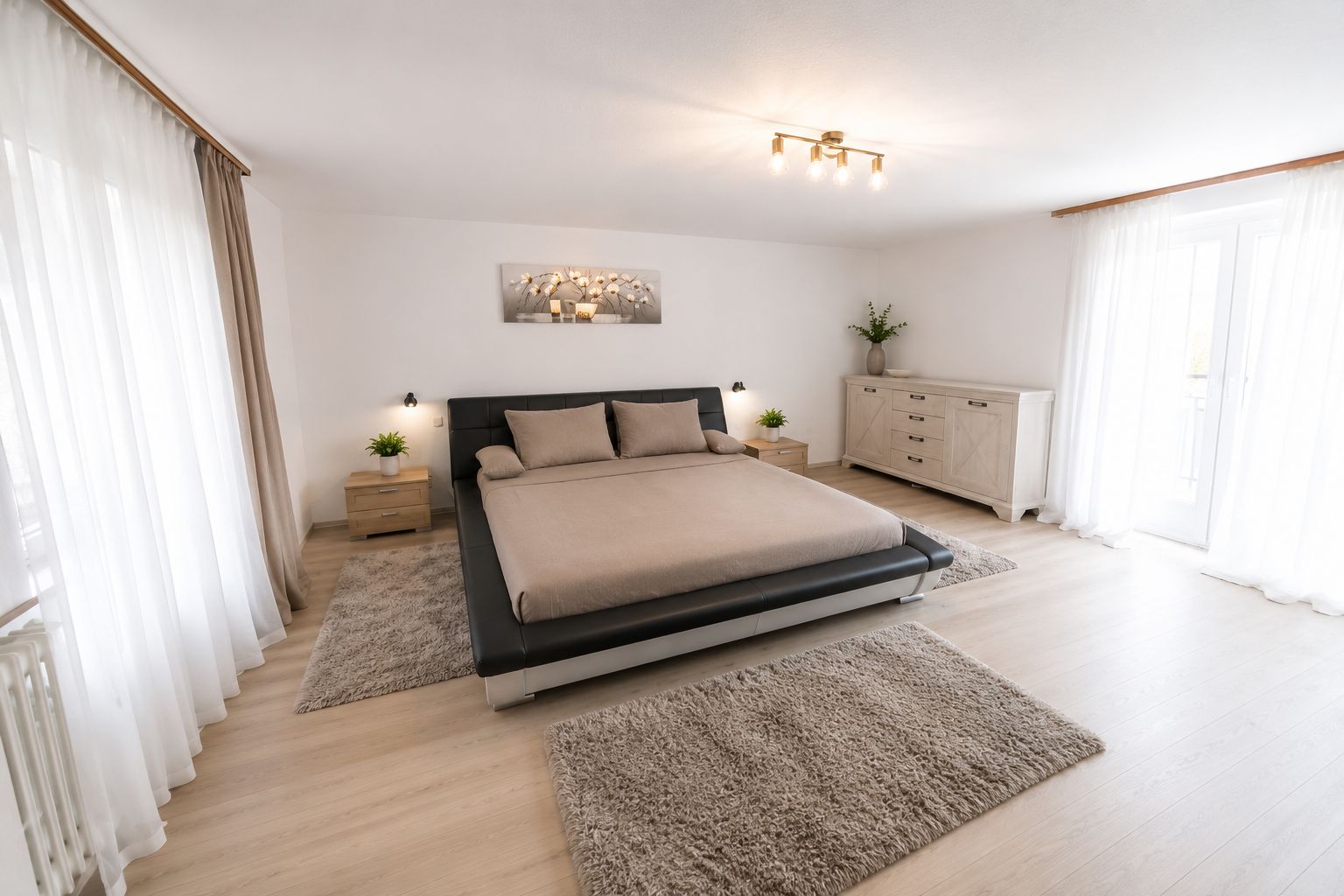Helles Schlafzimmer mit Doppelbett, Teppichen, Nachttischen und Kommode, Tageslicht durch große Fenster.